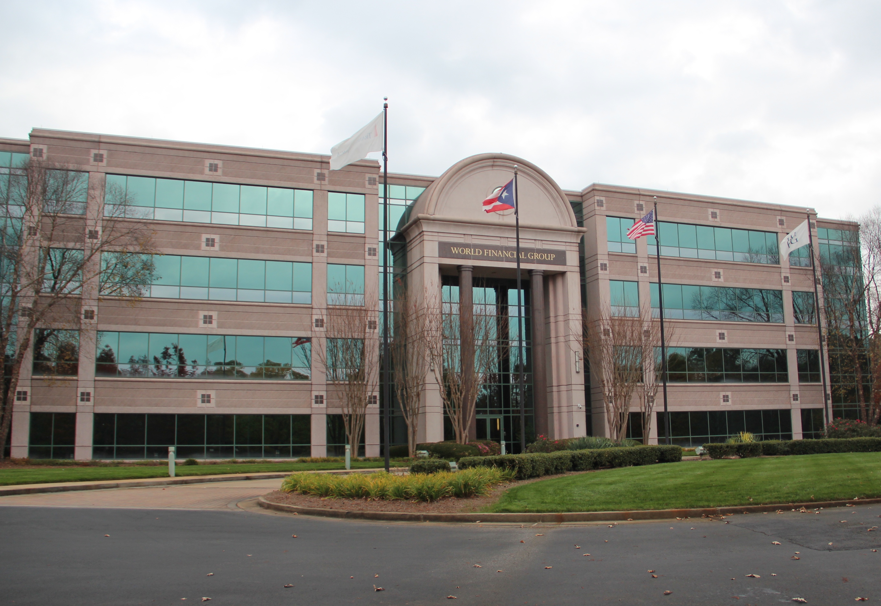Three-story tan brick office building with arched entrance and circular driveway.