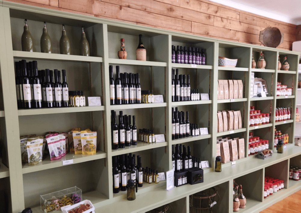 Sage-green shelving units lined with dark glass bottles and packaged food products in a wood-paneled shop.