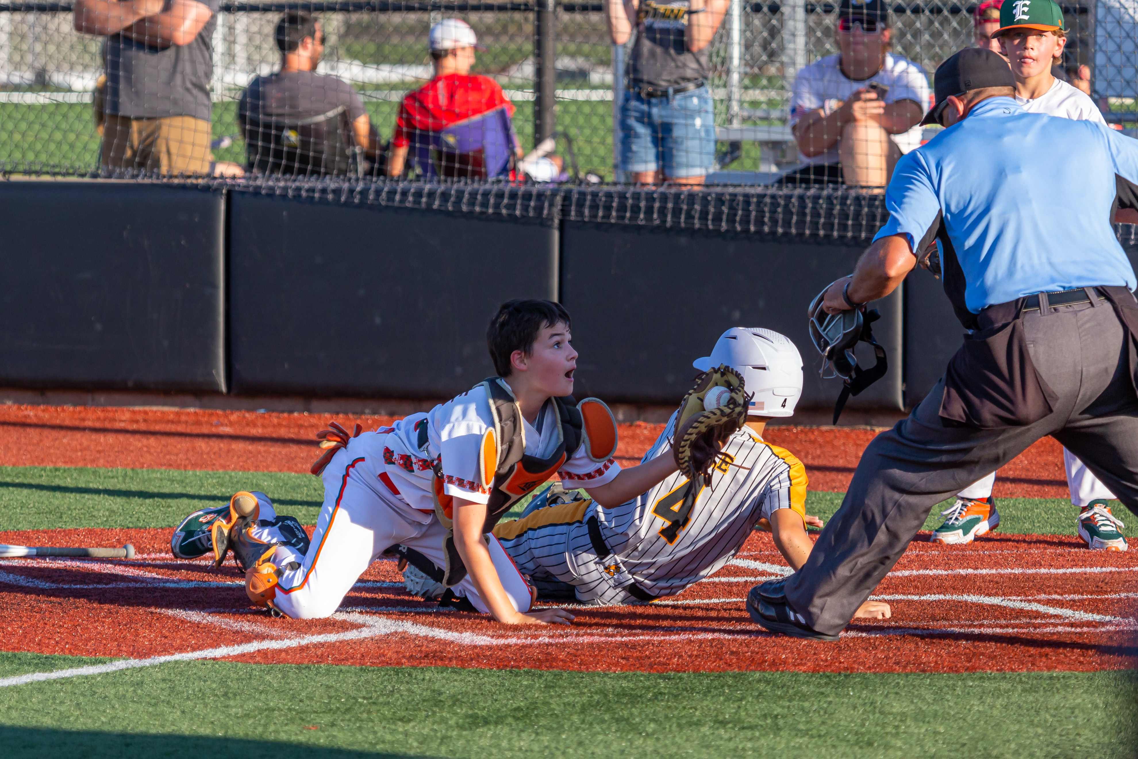 Youth baseball catcher tags out a sliding runner at home plate as an umpire watches.