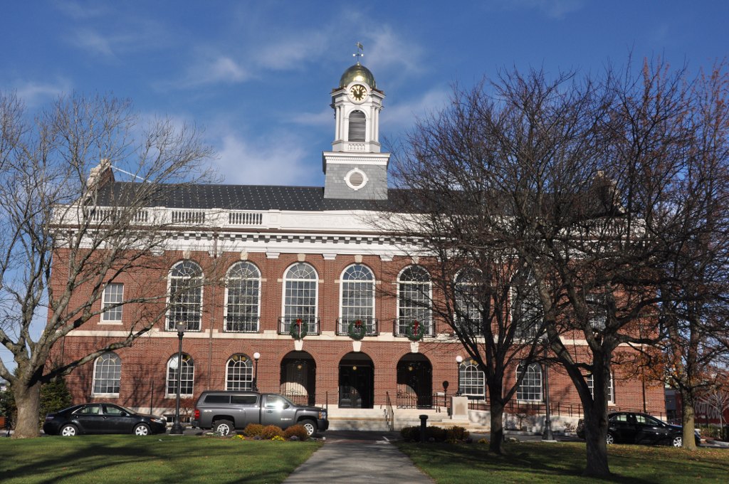 Red-brick colonial town hall building with white cupola, clock, and solar panels on roof.