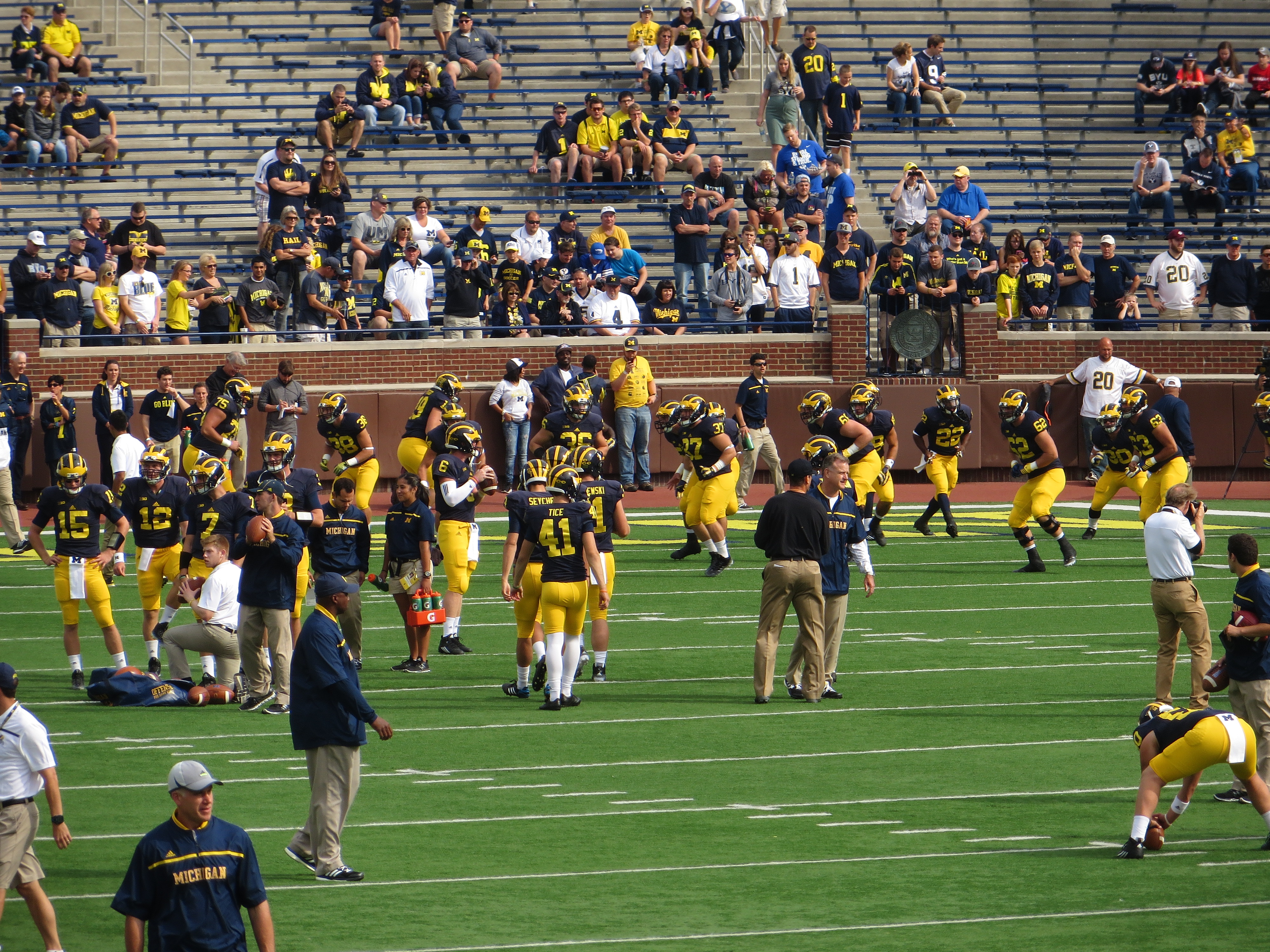 College football players in helmets and pads walking onto a large stadium field.