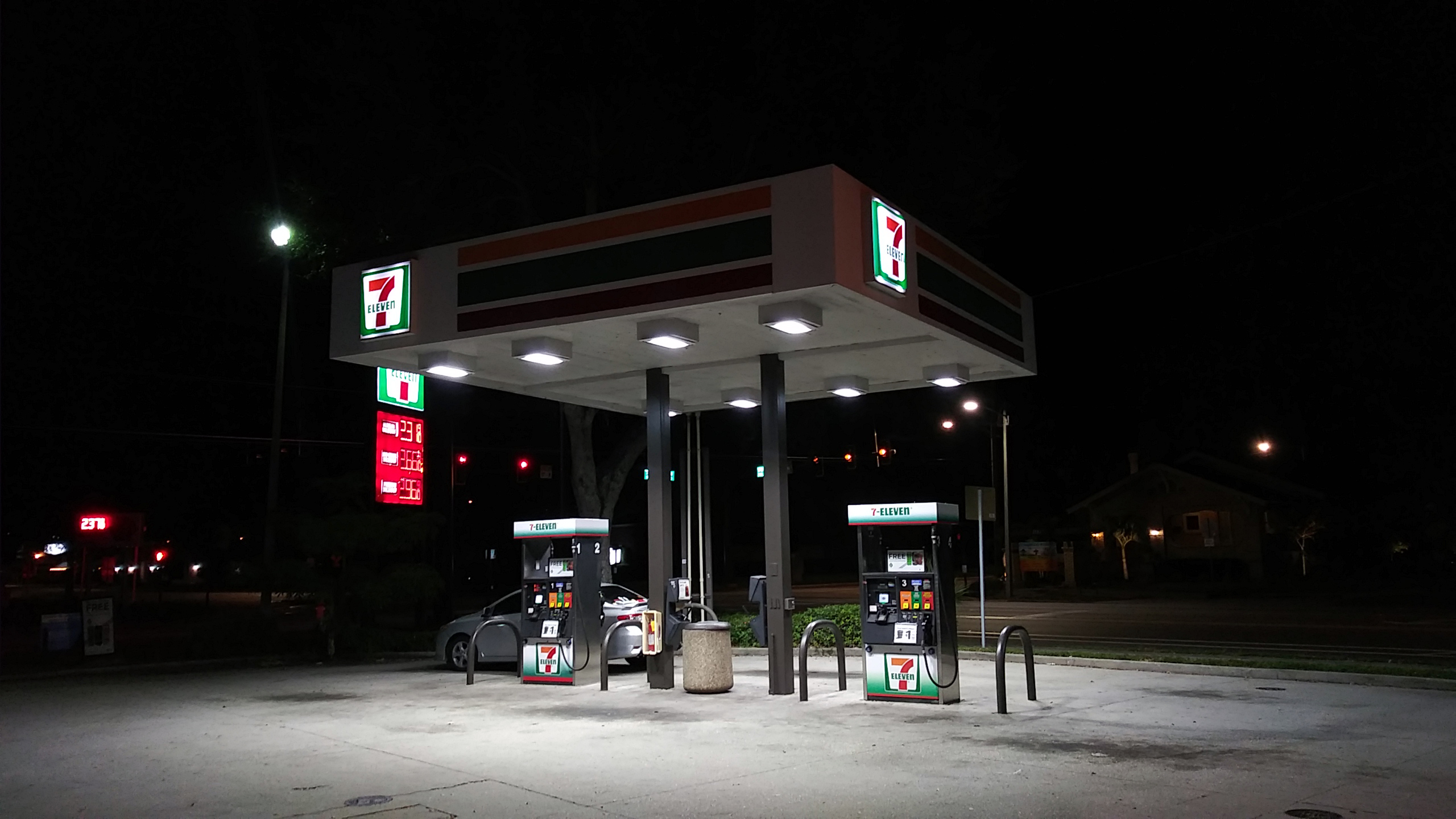 Illuminated gas station canopy with multiple fuel pump islands at night.