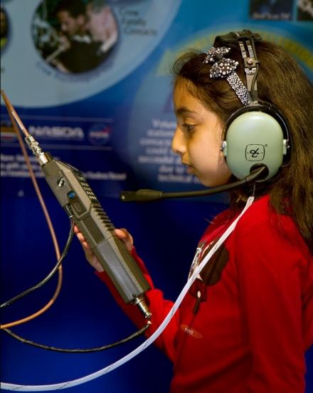 Student wearing headphones and holding a handheld radio in front of a NASA and ARISS display board.