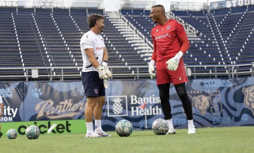 Two goalkeepers in training gear face each other on a soccer field in an empty stadium.