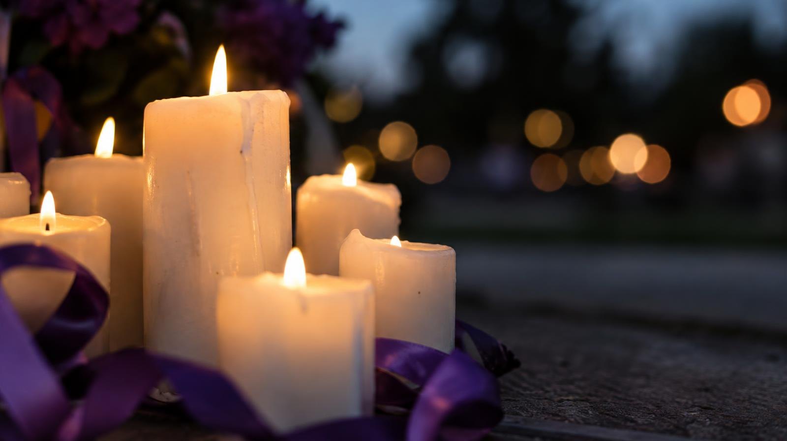 Cluster of lit white candles glowing softly beside a purple ribbon.