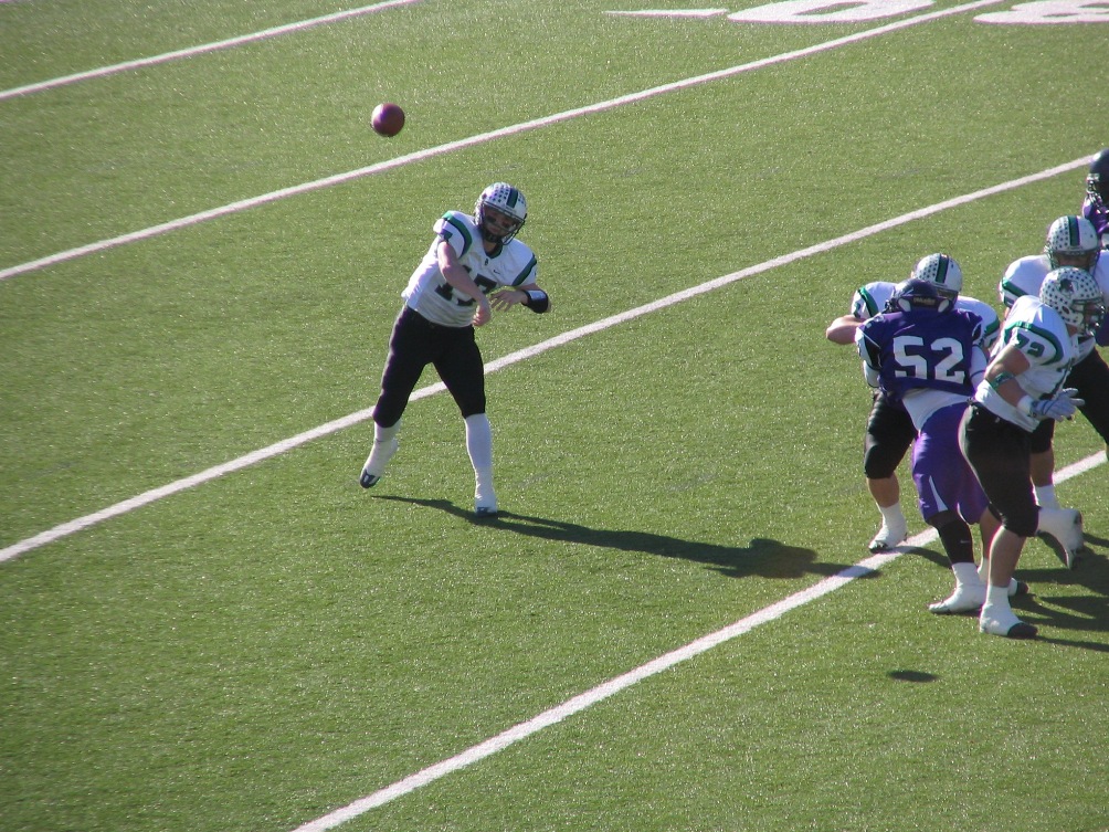 A quarterback in a white uniform throws a pass during a high school football game.