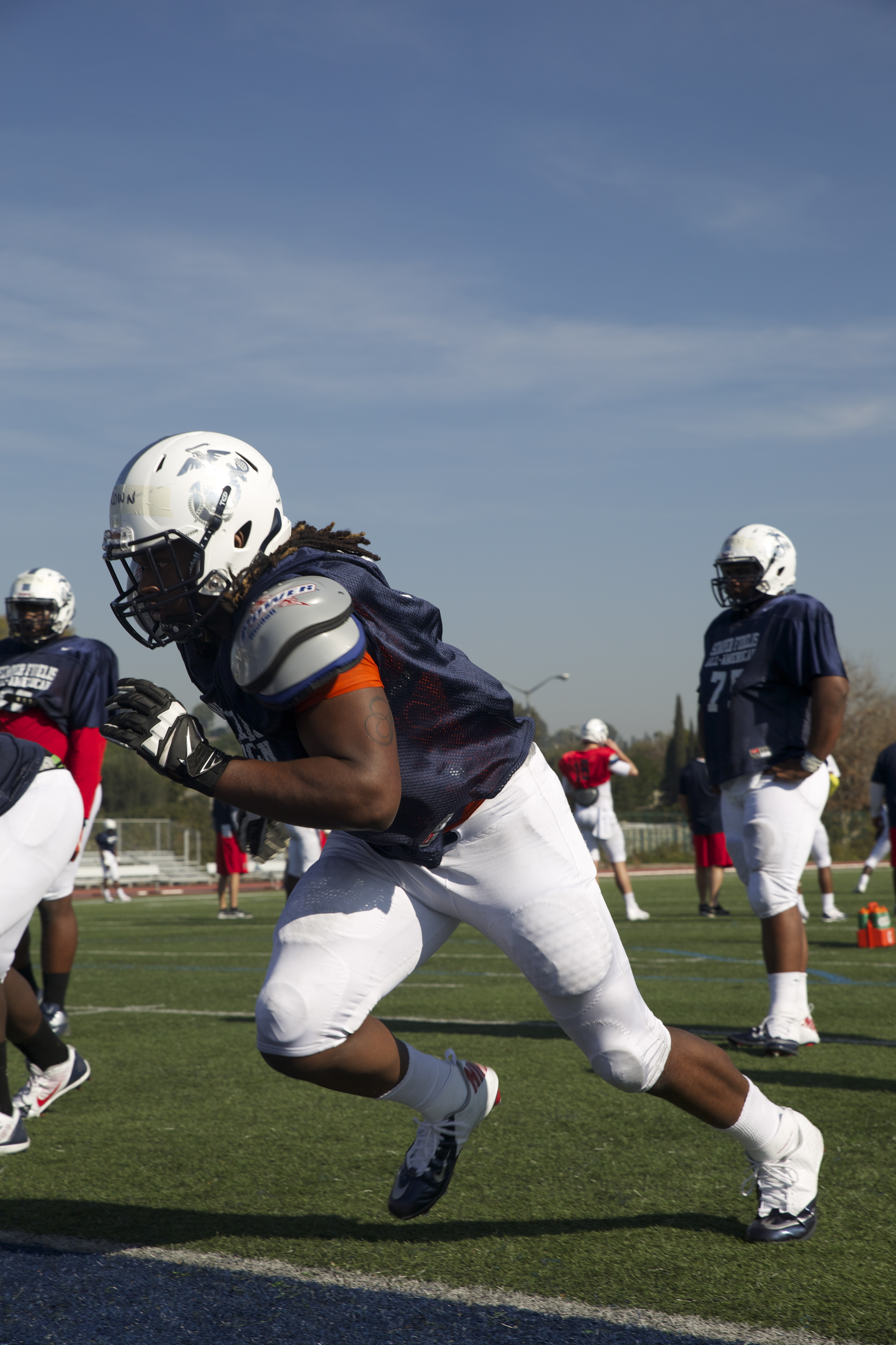 A football player in a white helmet and navy uniform runs a drill on a practice field.