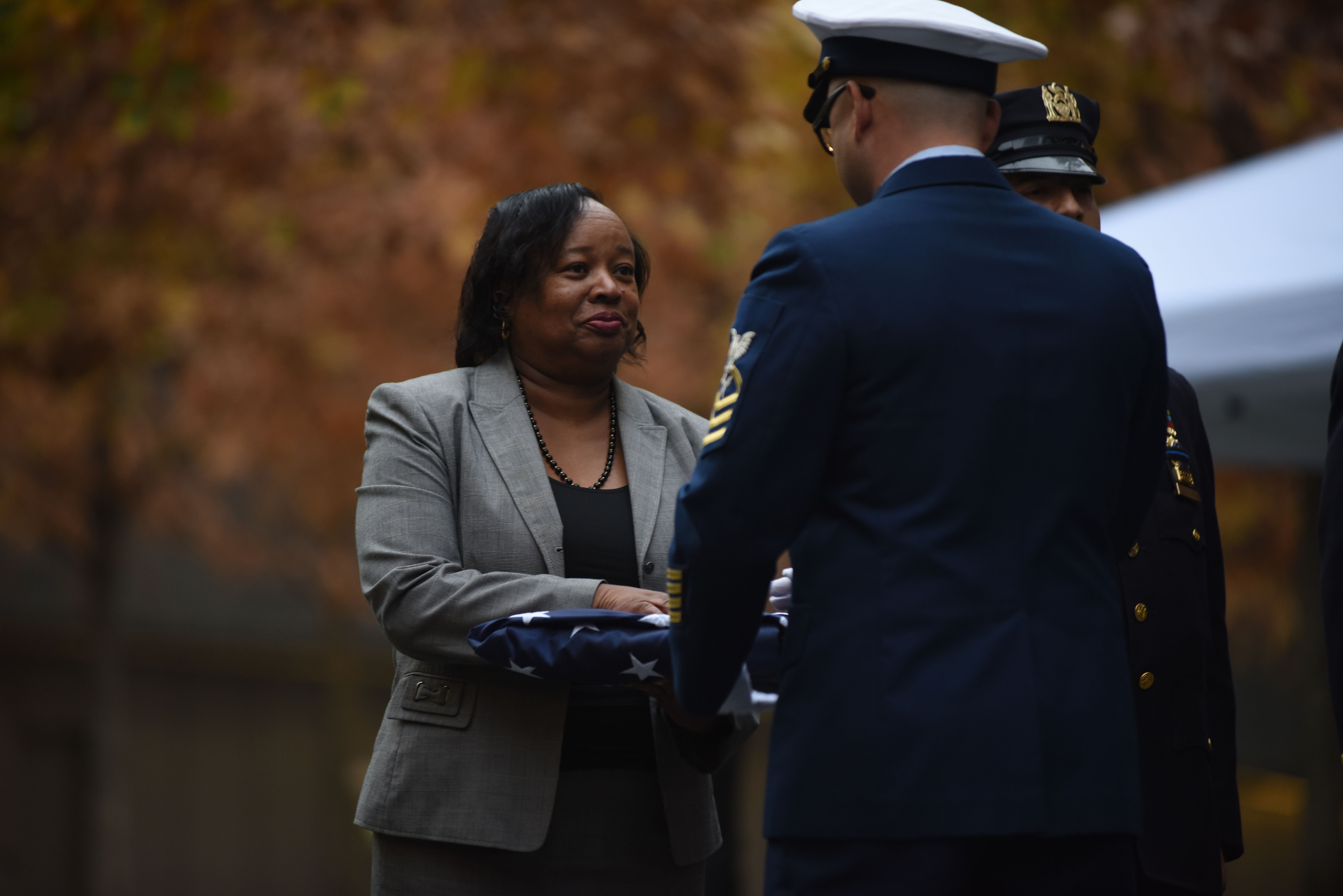 A uniformed military officer presents a folded American flag to a woman at an outdoor ceremony.