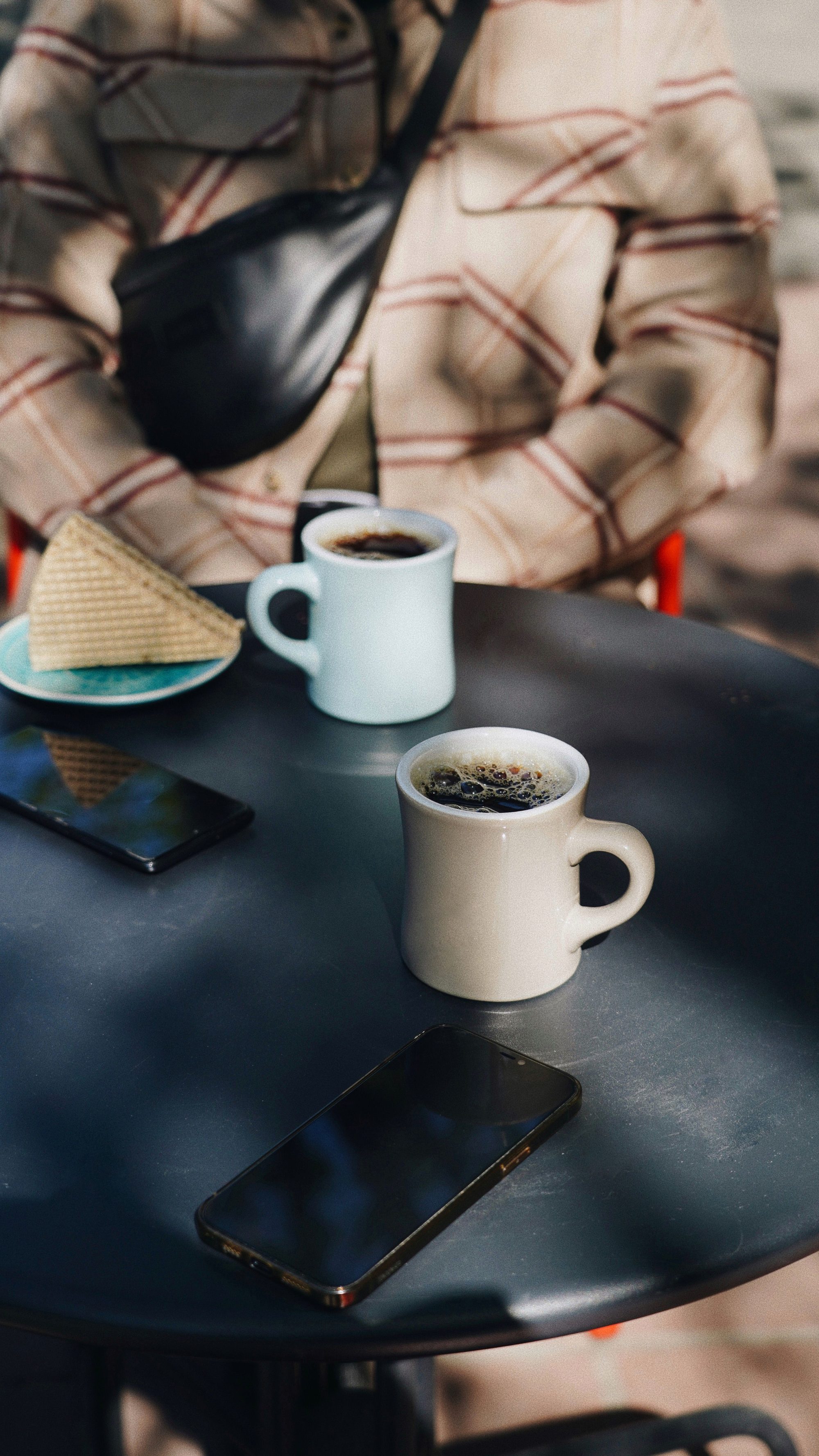 Two ceramic mugs and smartphones on an outdoor table, highlighting a casual coffee break atmosphere.