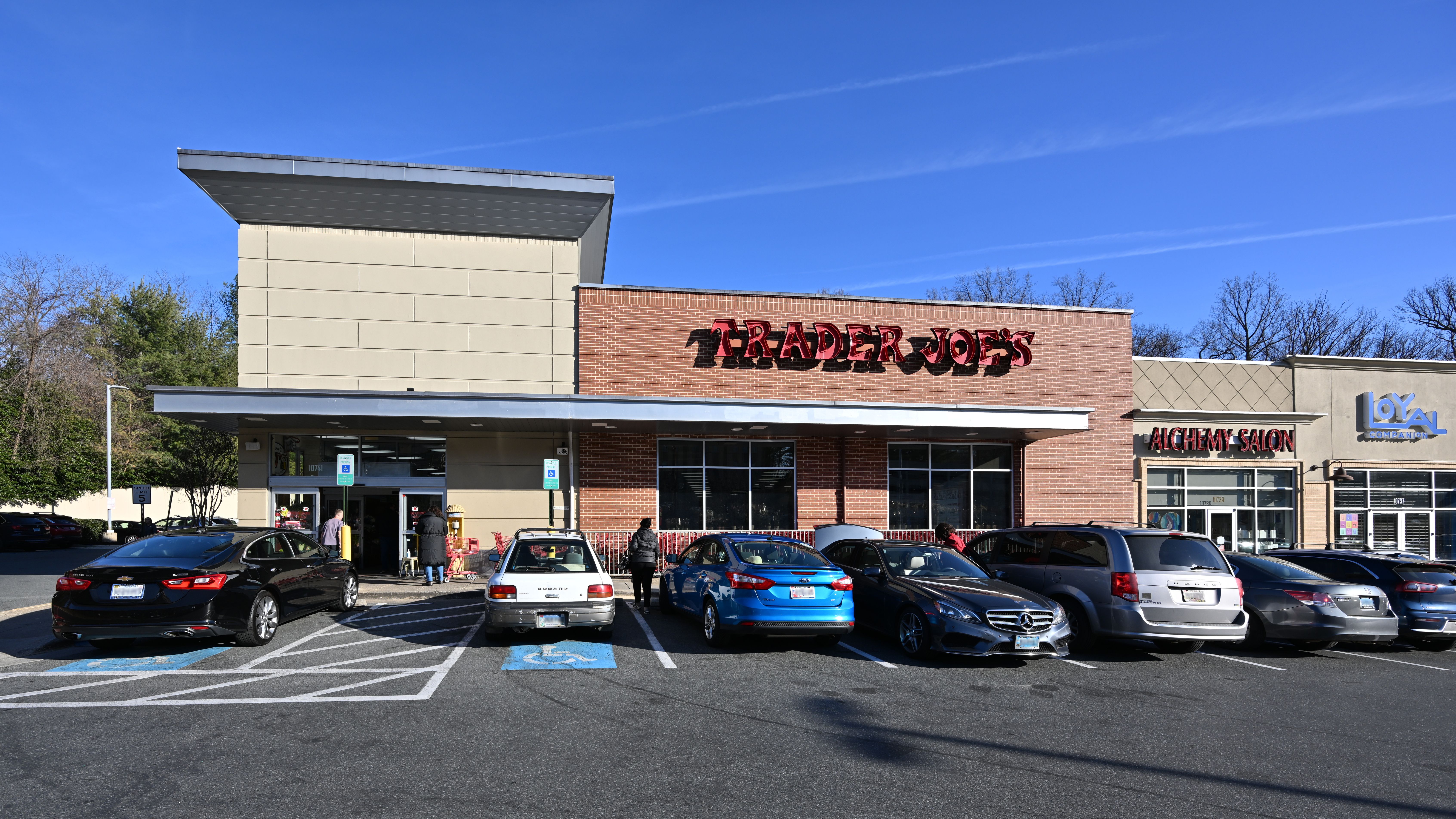 Exterior of a Trader Joe's grocery store in a strip mall with cars parked in front.