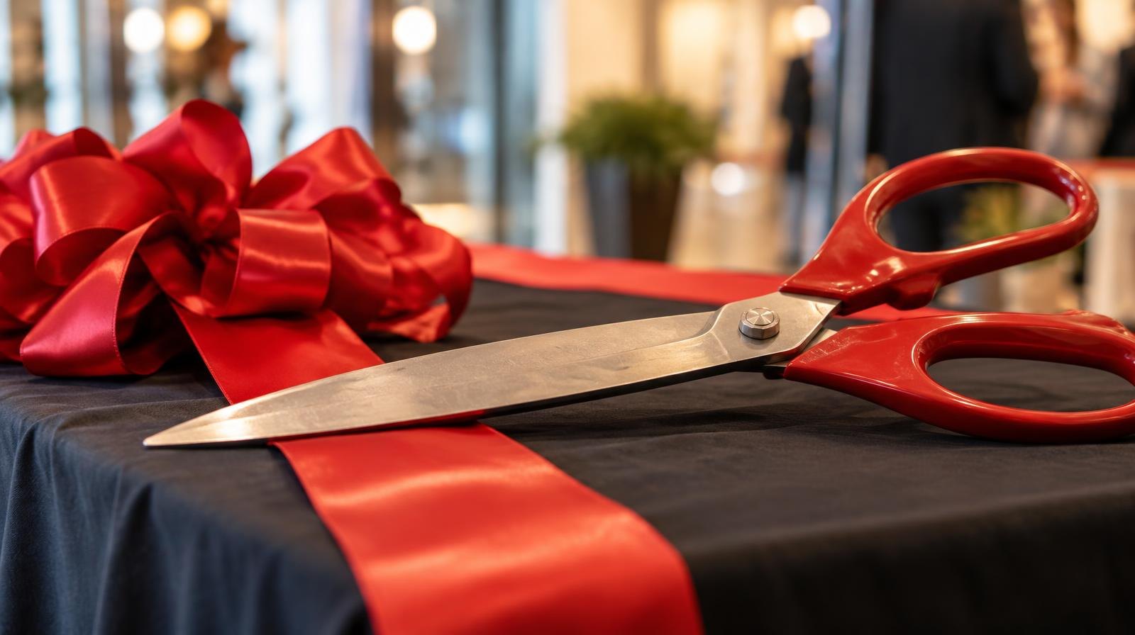 Large ceremonial scissors resting beside a red satin ribbon bow.