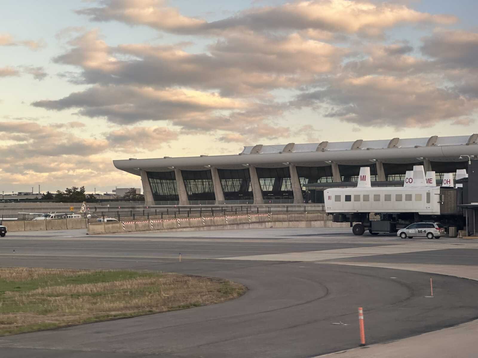 Mobile lounges parked on an airport tarmac with a curved terminal building behind them.
