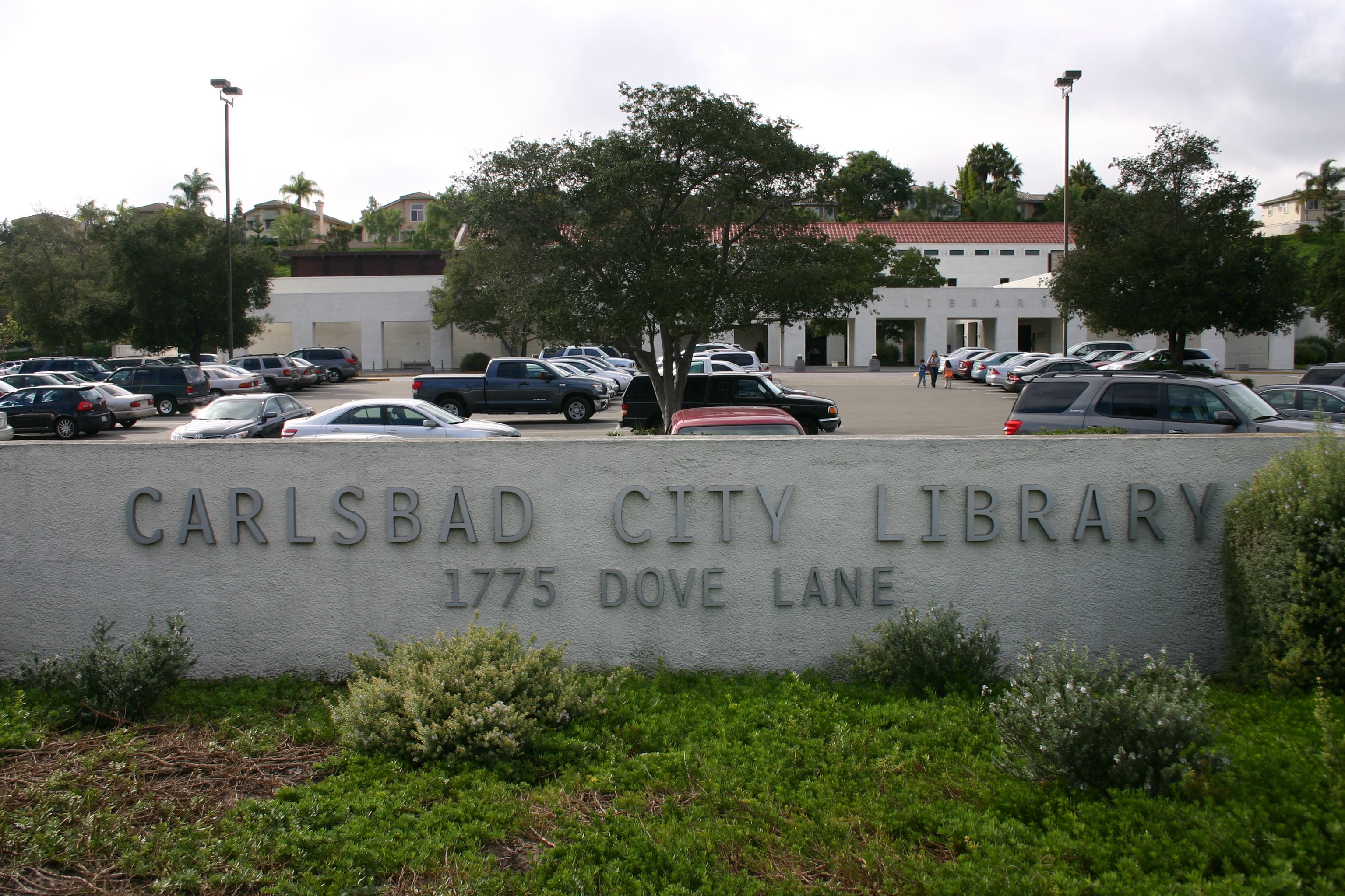 Stone sign reading Carlsbad City Library at 1775 Dove Lane, with the library building behind it.