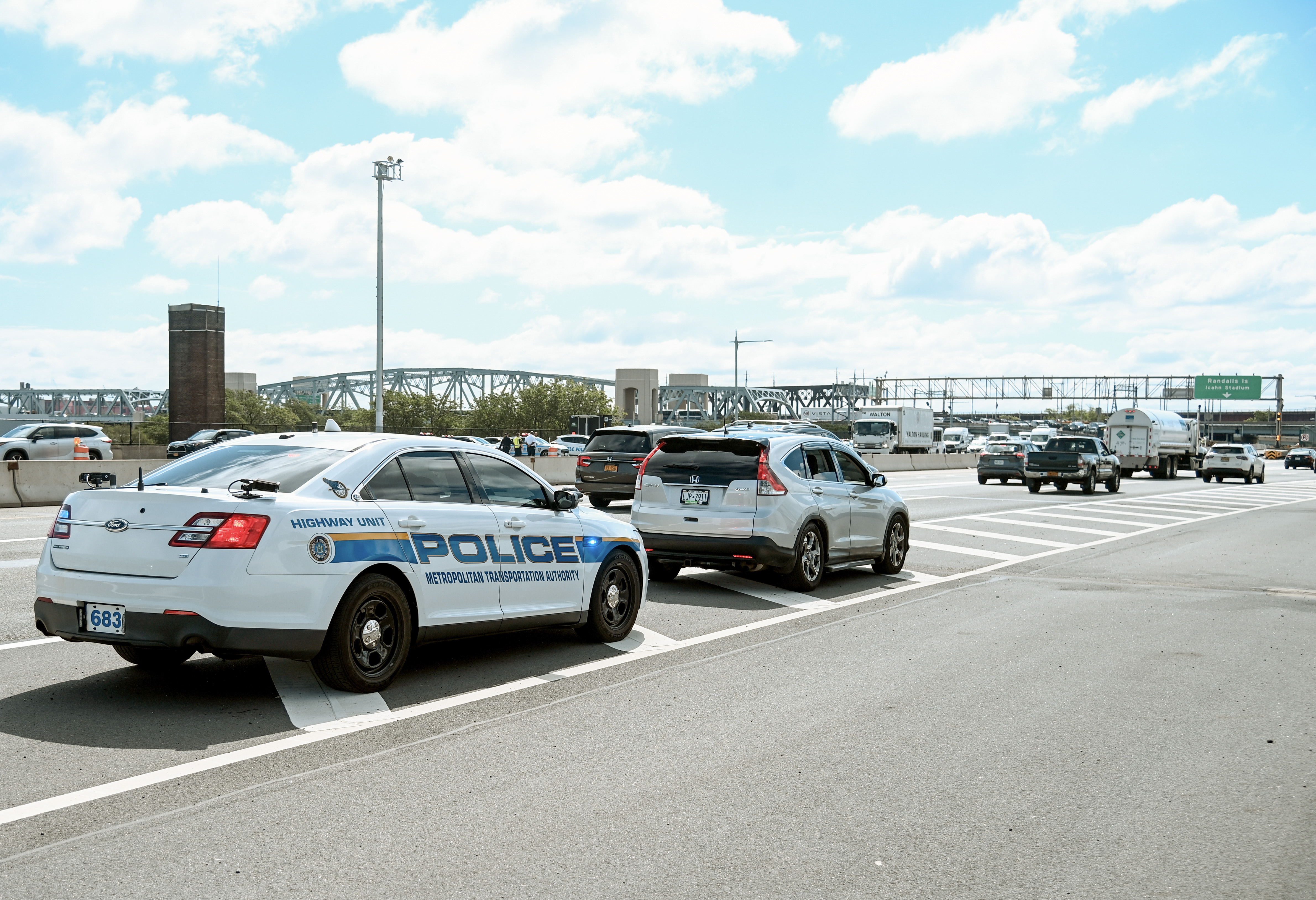 A white police patrol car parked on a roadway during a traffic enforcement operation near a bridge.