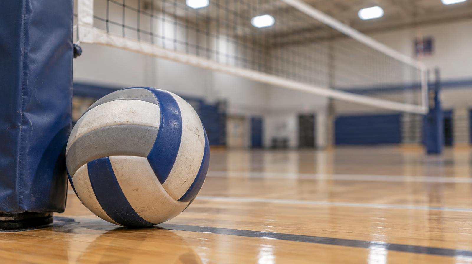 A volleyball resting on a gym floor next to a net post.
