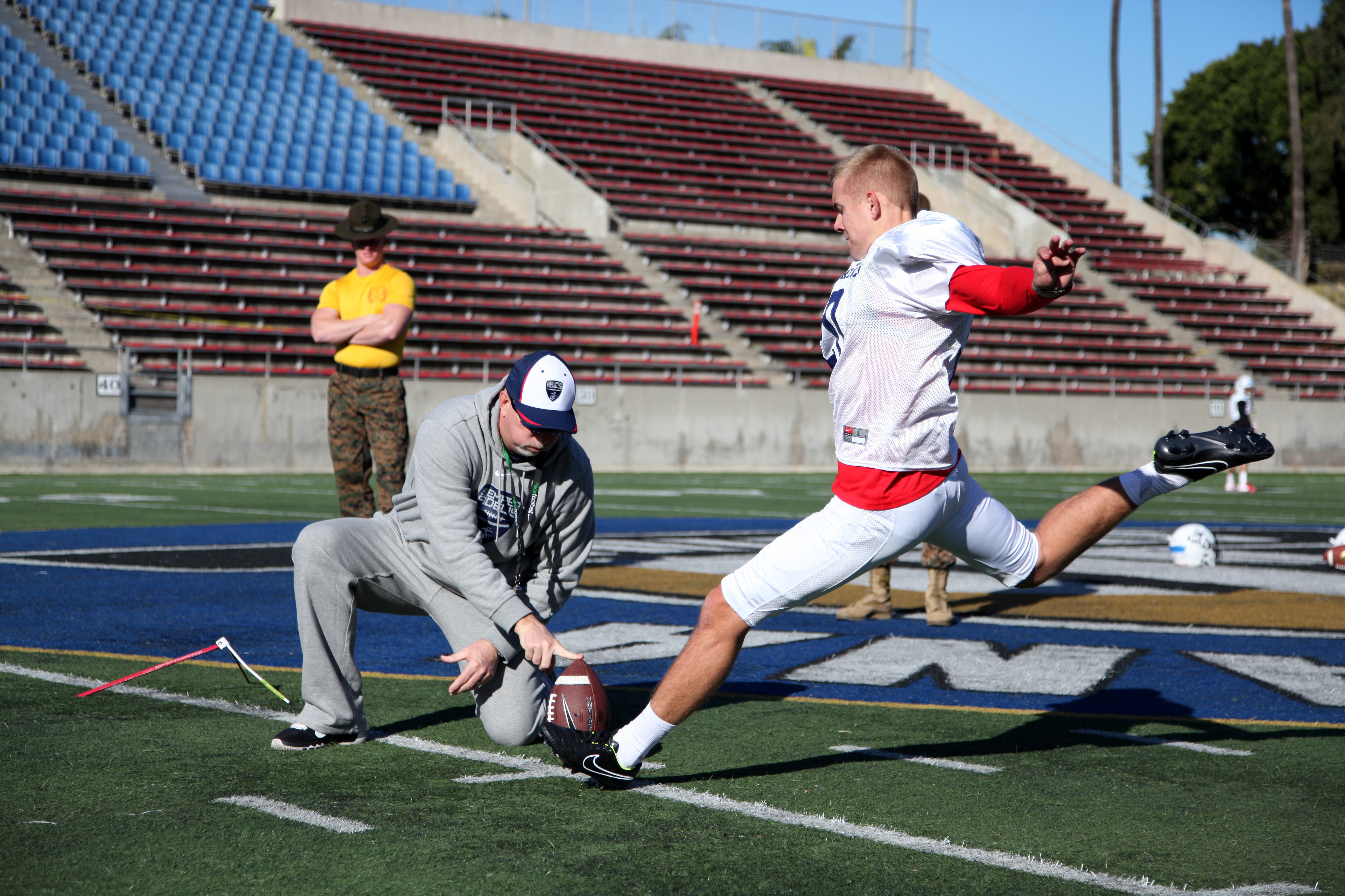 A football kicker mid-motion executing a field goal kick, holder crouching nearby.