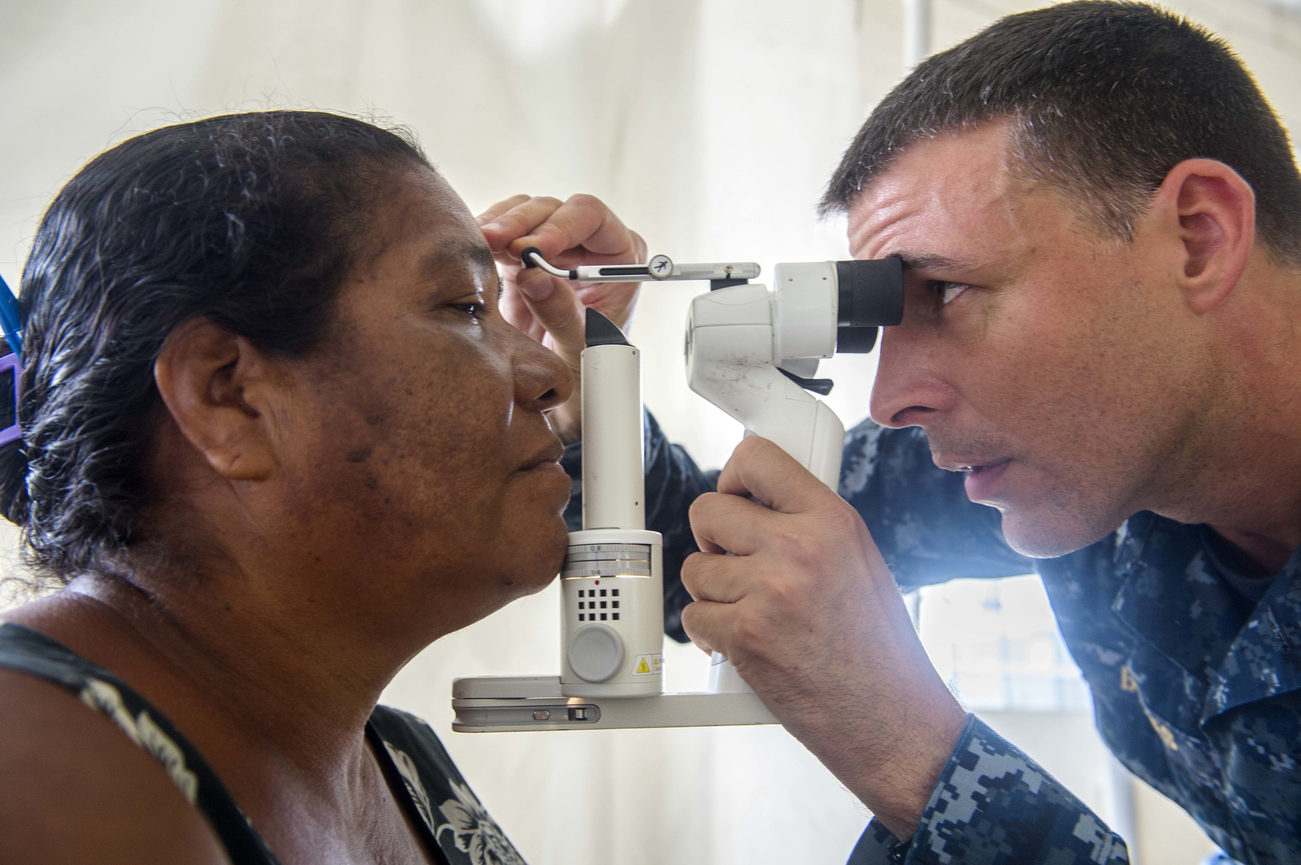 Optometrist uses a handheld instrument to examine a seated patient's eye.