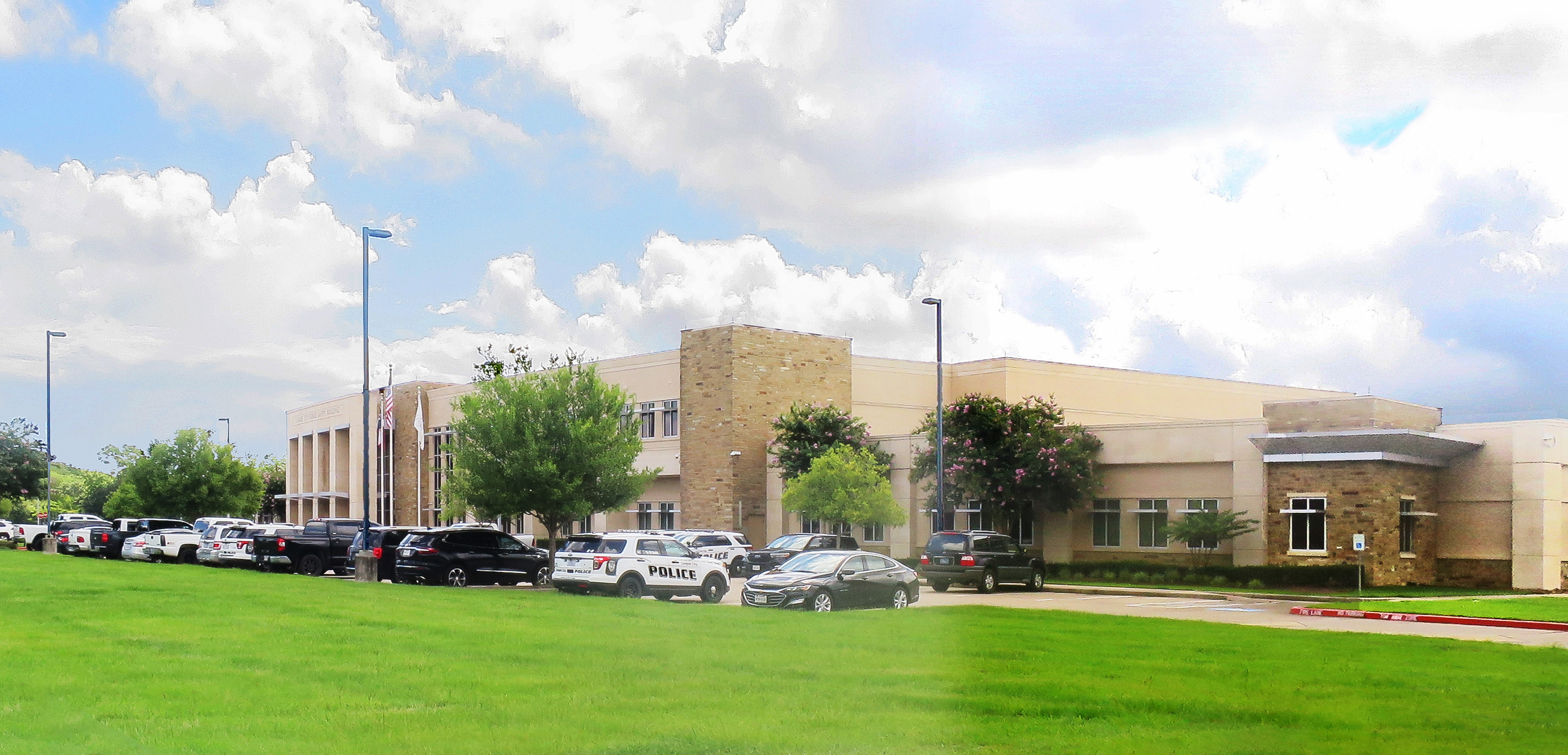 Large modern tan police department building with patrol vehicles parked out front.