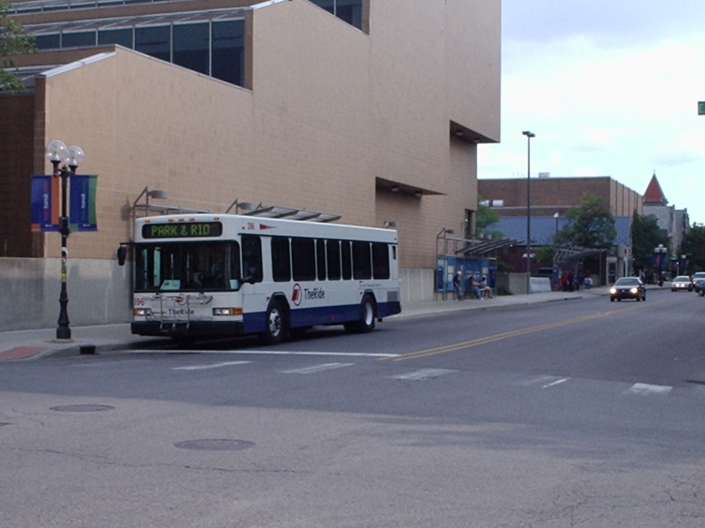A TheRide bus on a city street with the Blake Transit Center visible in the background.