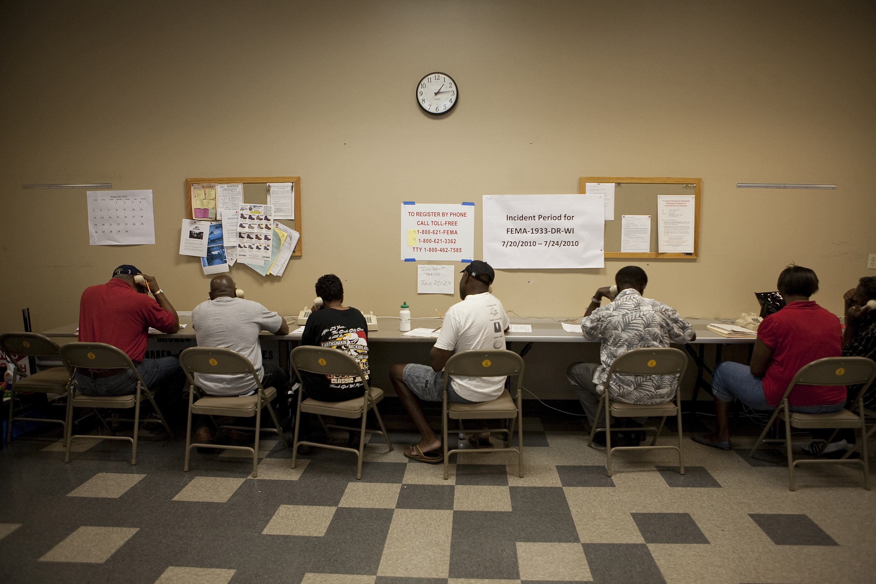 People seated at a long table using phones inside a FEMA disaster recovery center.