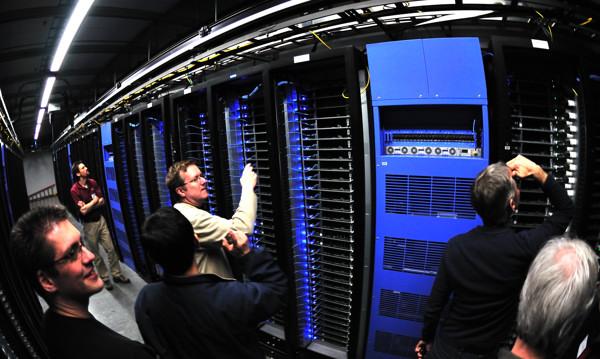 People examining rows of blue-lit server racks inside a large data center.