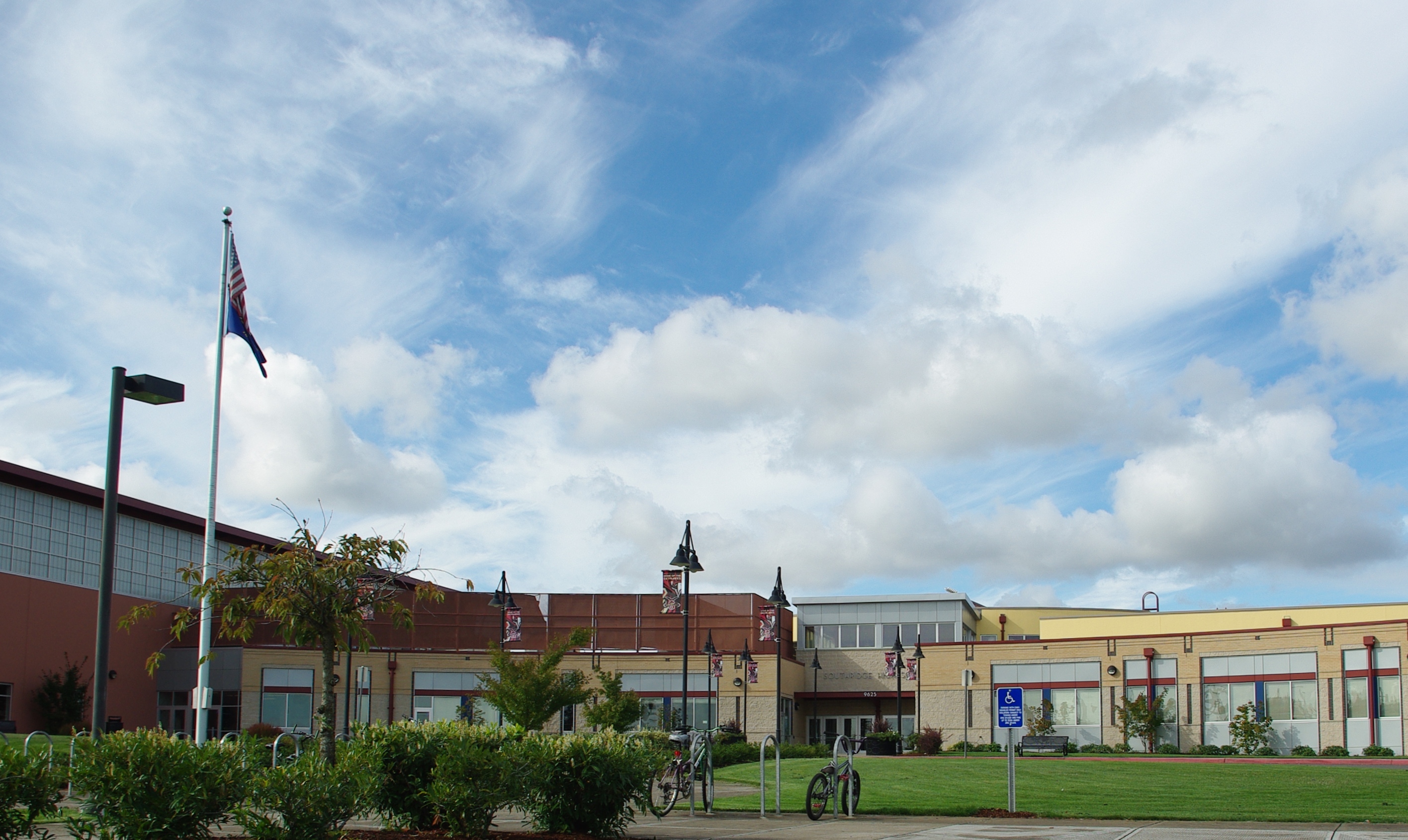 Exterior of a school campus with a flagpole, green lawn, and low-rise buildings.