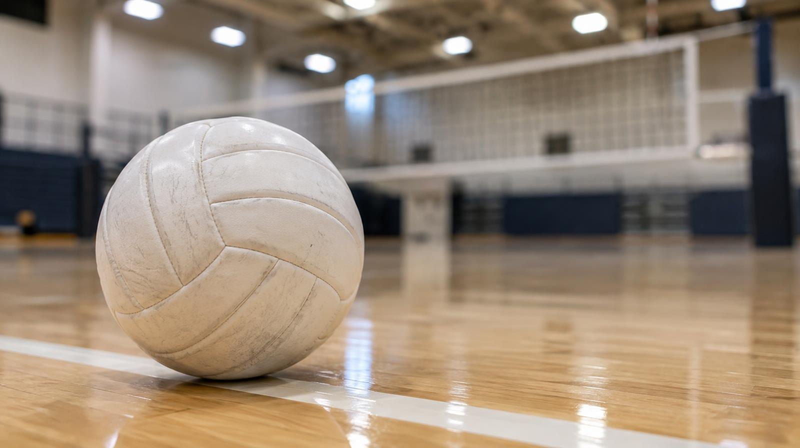 White volleyball on a hardwood gym floor with a net blurred in the background.