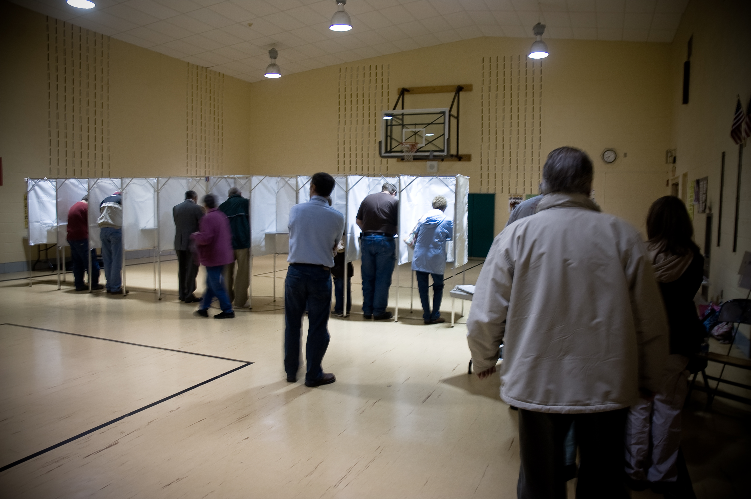Voters stand at white privacy booths inside a gymnasium used as a polling place.