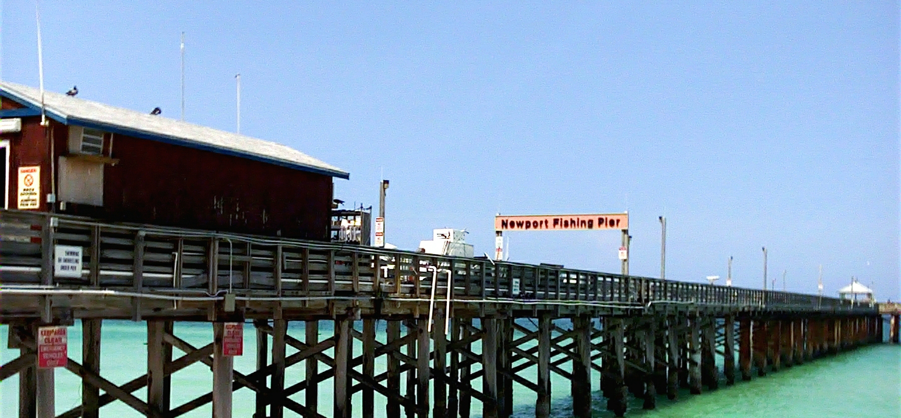 Newport Fishing Pier extending over turquoise ocean water under a clear blue sky.