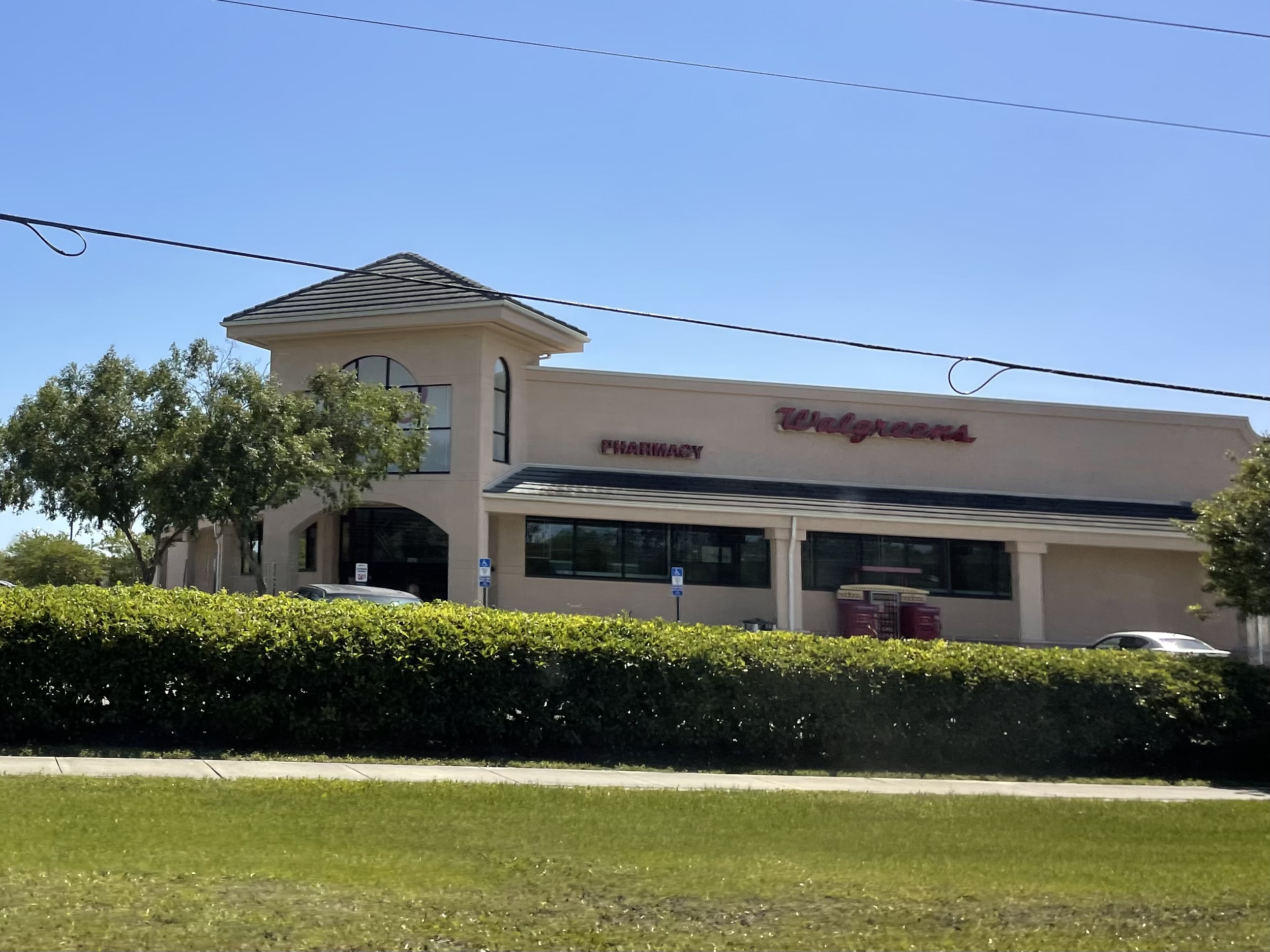 Exterior of a Walgreens pharmacy with beige stucco facade and green hedges.