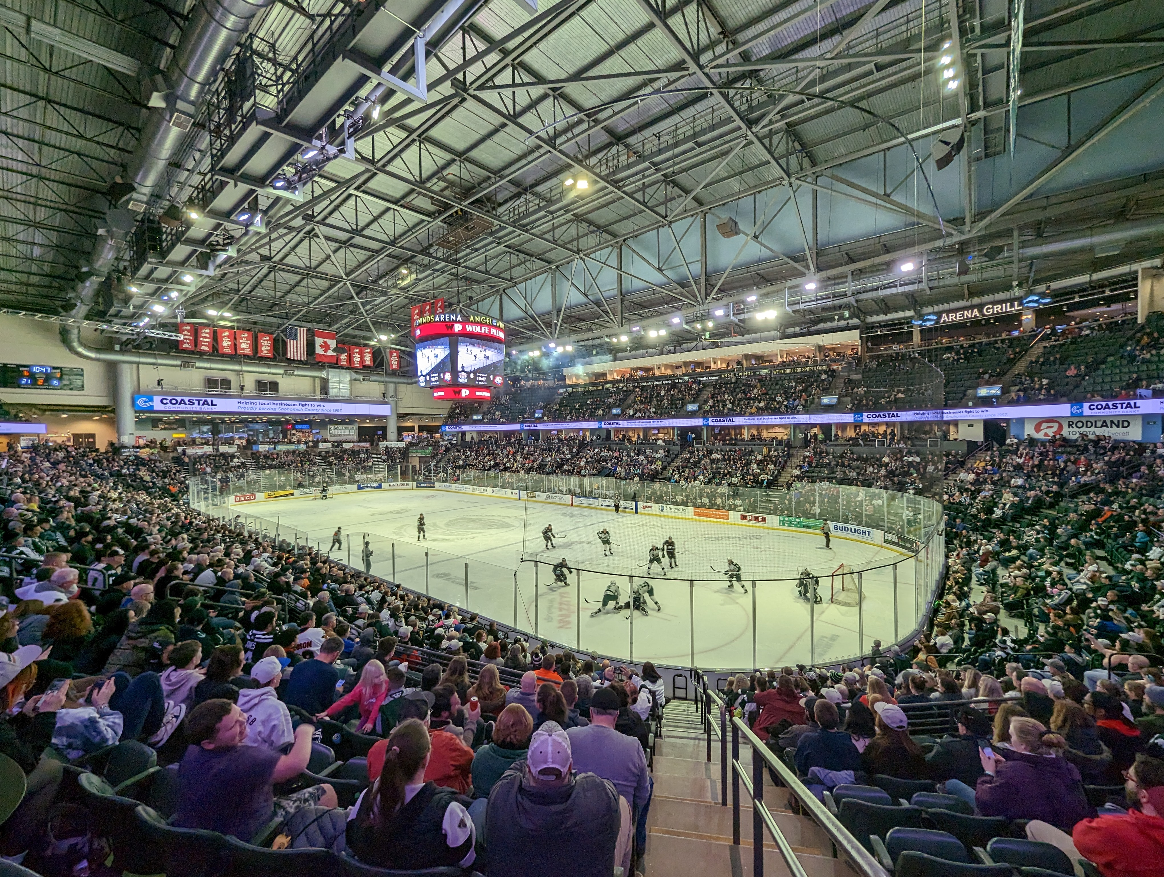 Packed indoor arena with spectators watching a hockey game on the ice below.