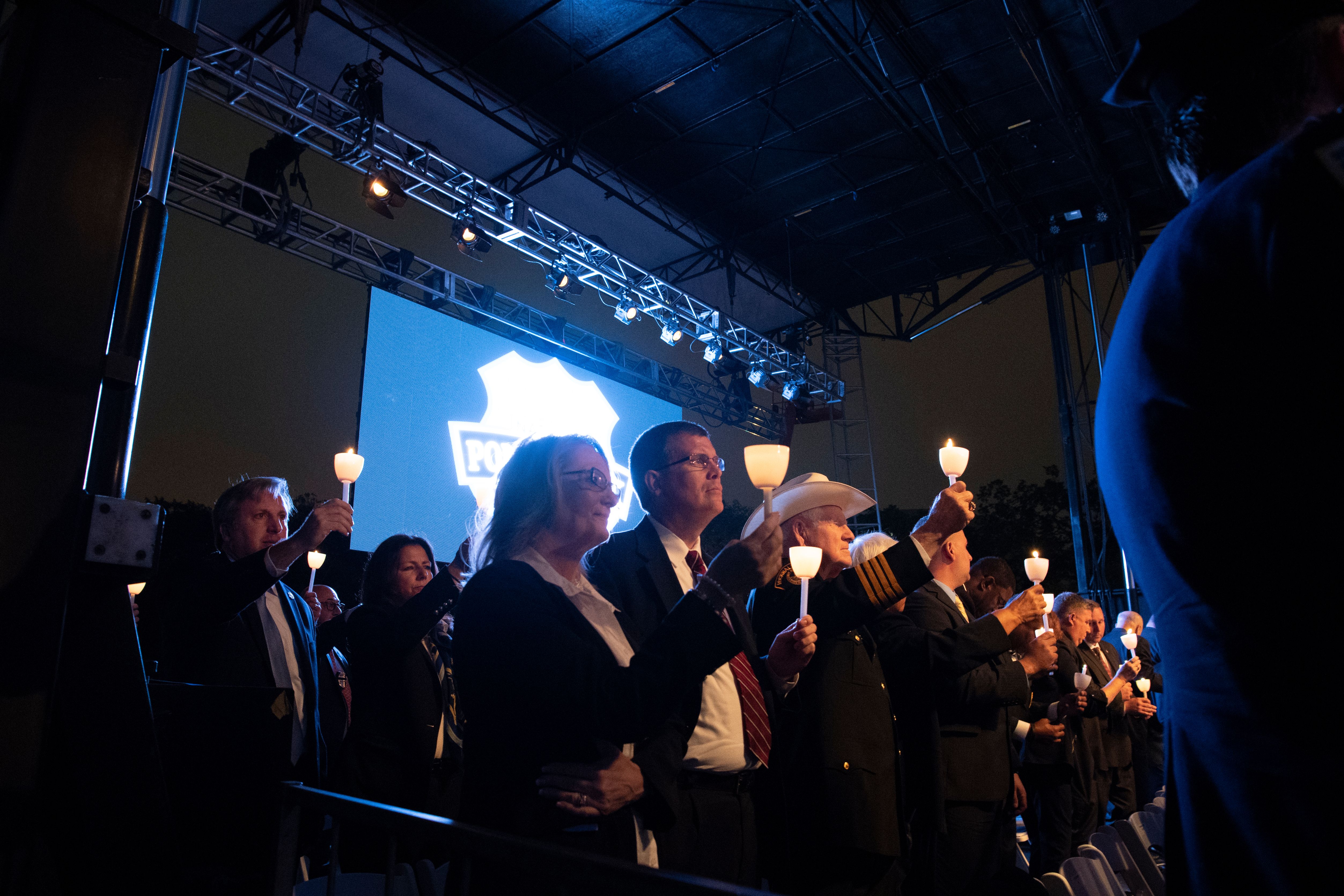 A row of people in formal attire holding lit candles at a vigil ceremony.