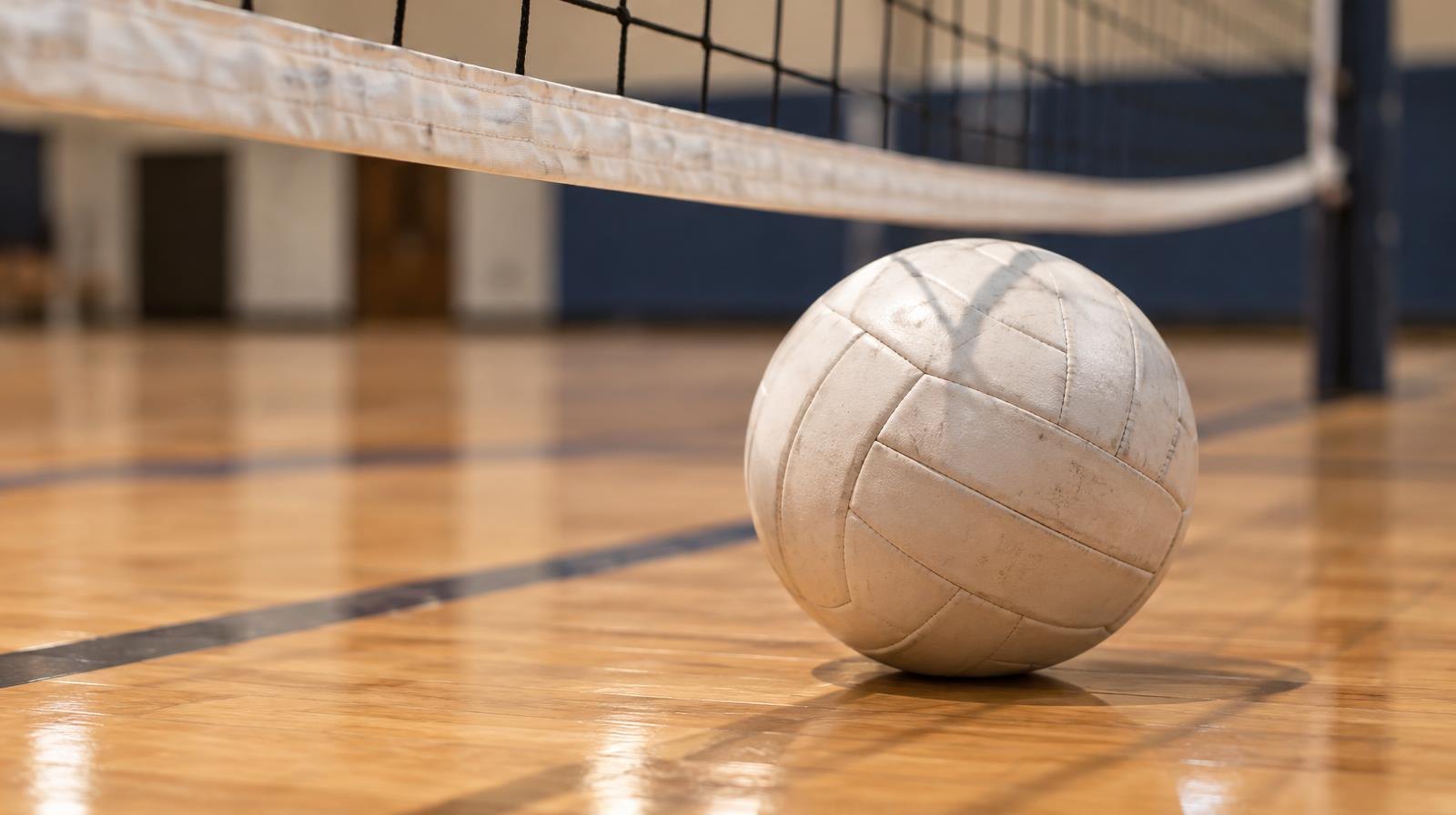 A white volleyball resting on a gymnasium floor near a net.