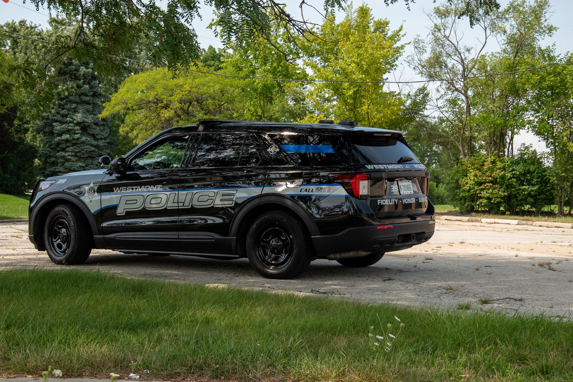 Black marked police SUV with roof light bar parked outdoors near trees.