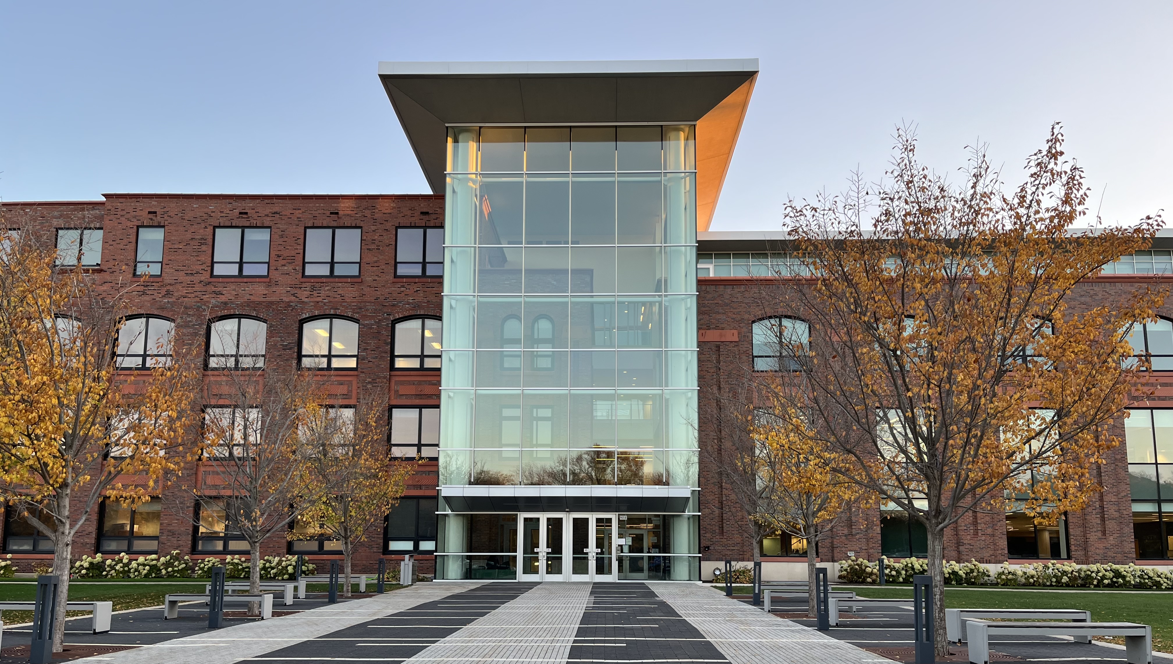 Glass atrium entrance of a large red brick high school building with autumn trees.