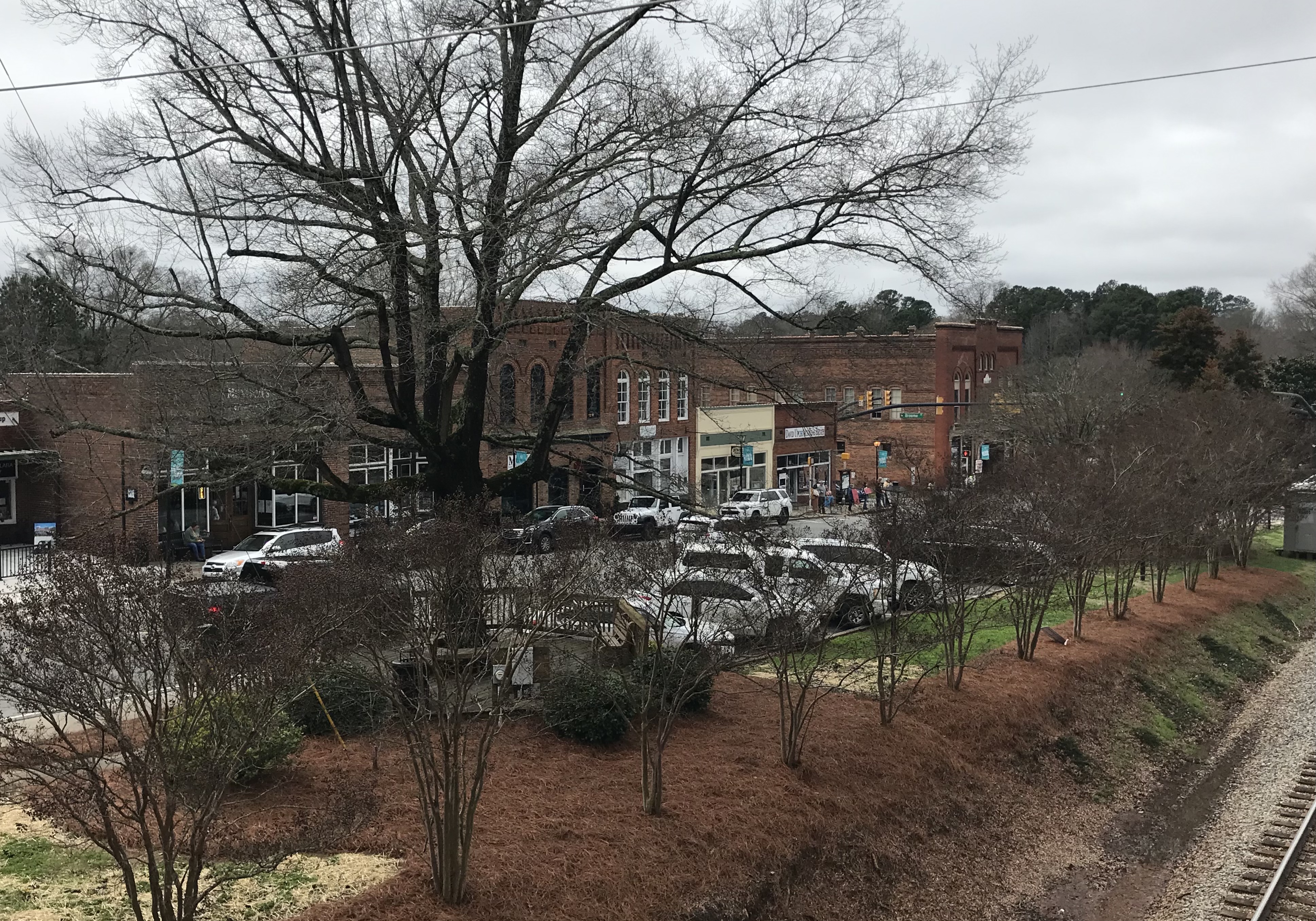 Aerial view of a small-town main street with brick storefronts and railroad tracks in the foreground.