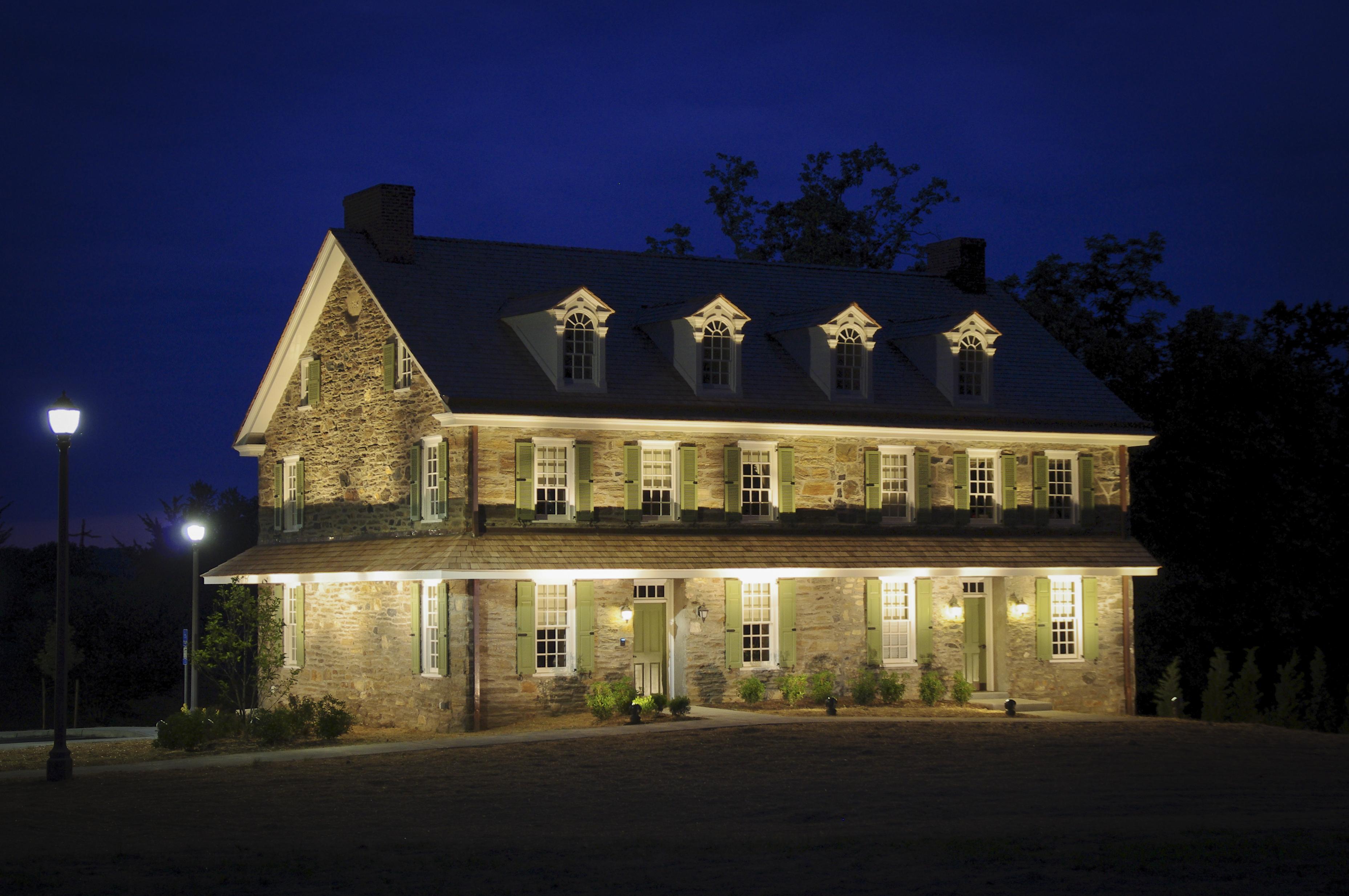 A two-story stone tavern building lit up at night with dormer windows and shutters.