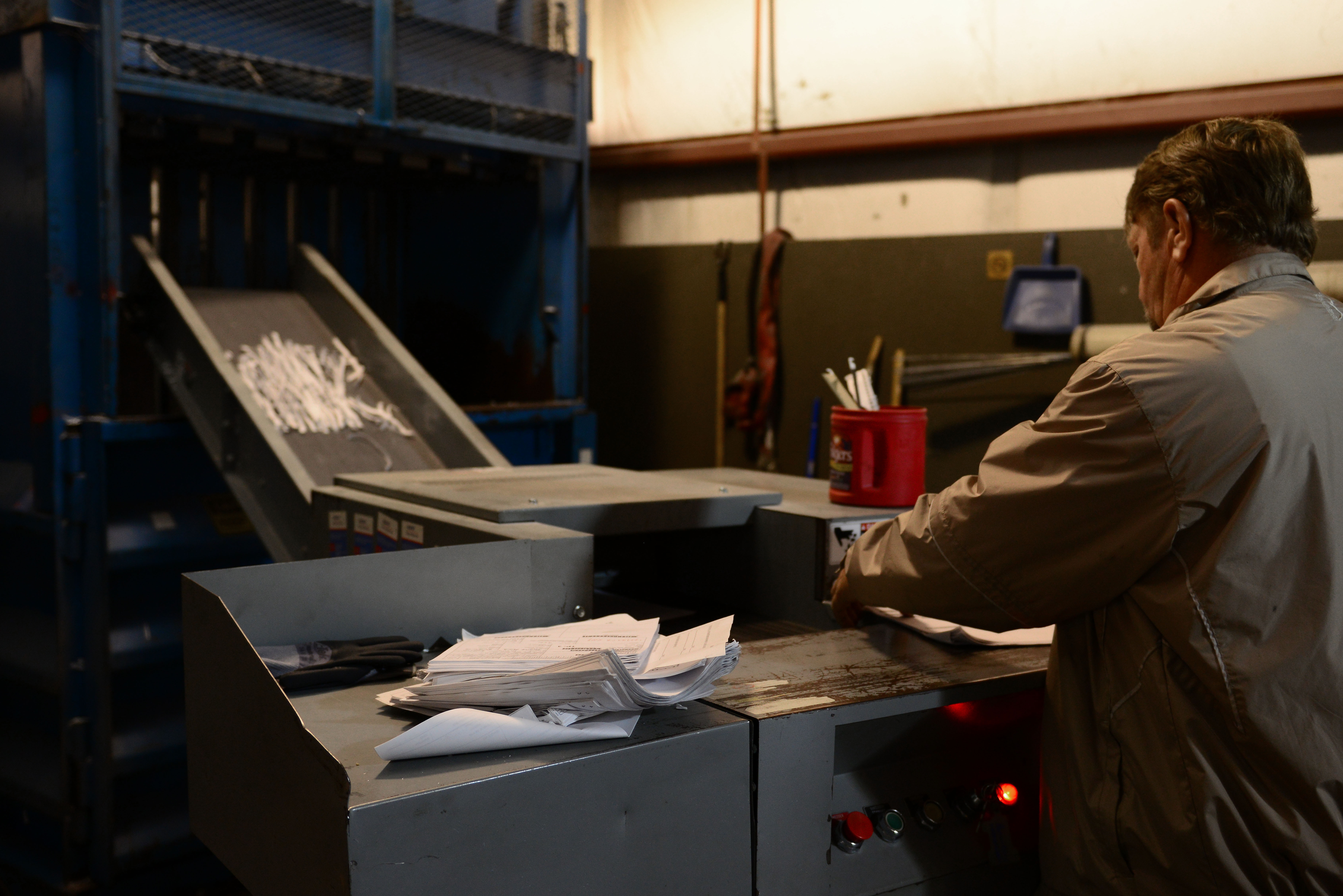 A man feeds papers into an industrial shredding machine at a recycling facility.