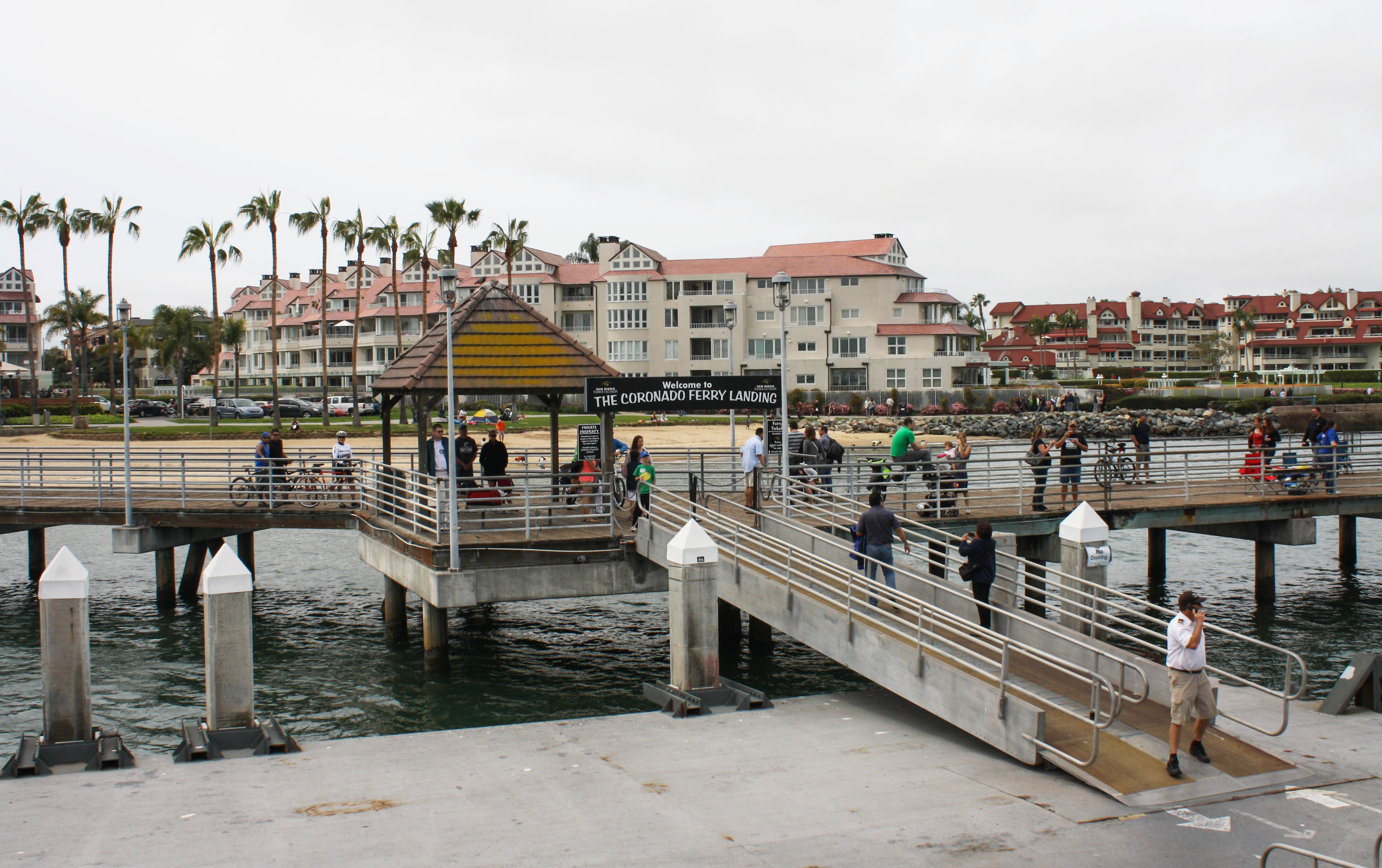 Pier entrance at Coronado Ferry Landing with a covered sign structure and palm trees.