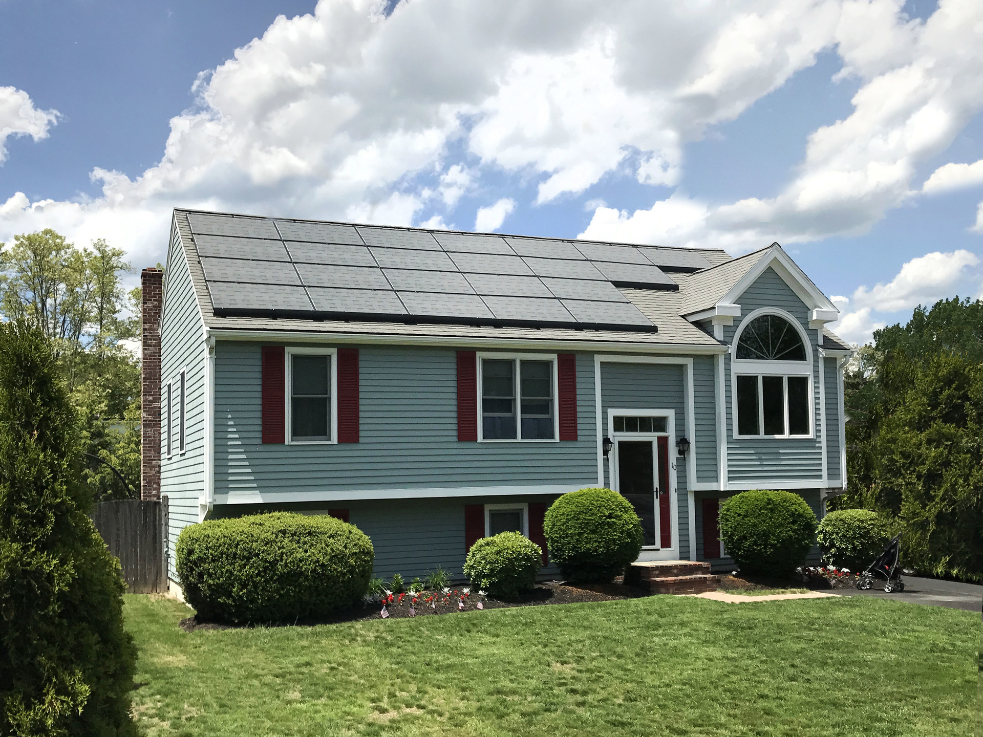 A residential home with solar panels on its roof and a green front lawn.