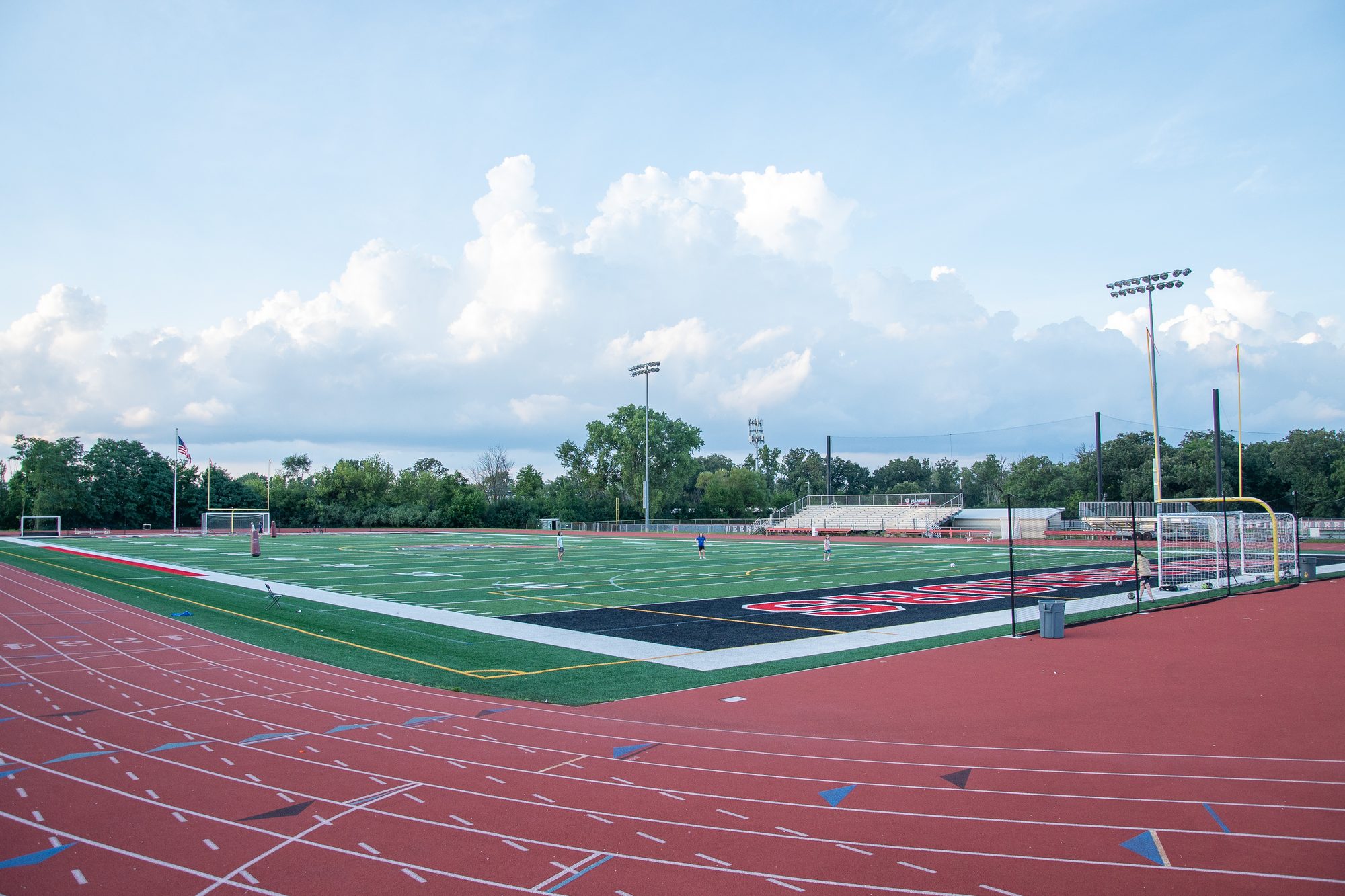 Artificial turf sports field with a soccer goal, red running track, and stadium lights.