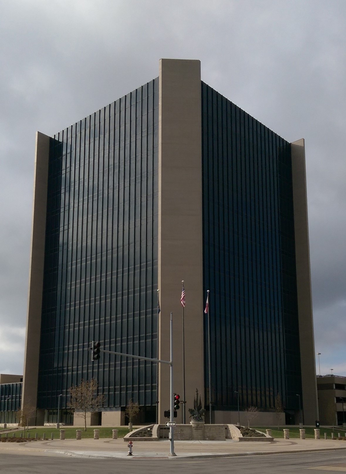 Modernist glass and steel city hall building with flagpoles under an overcast sky.