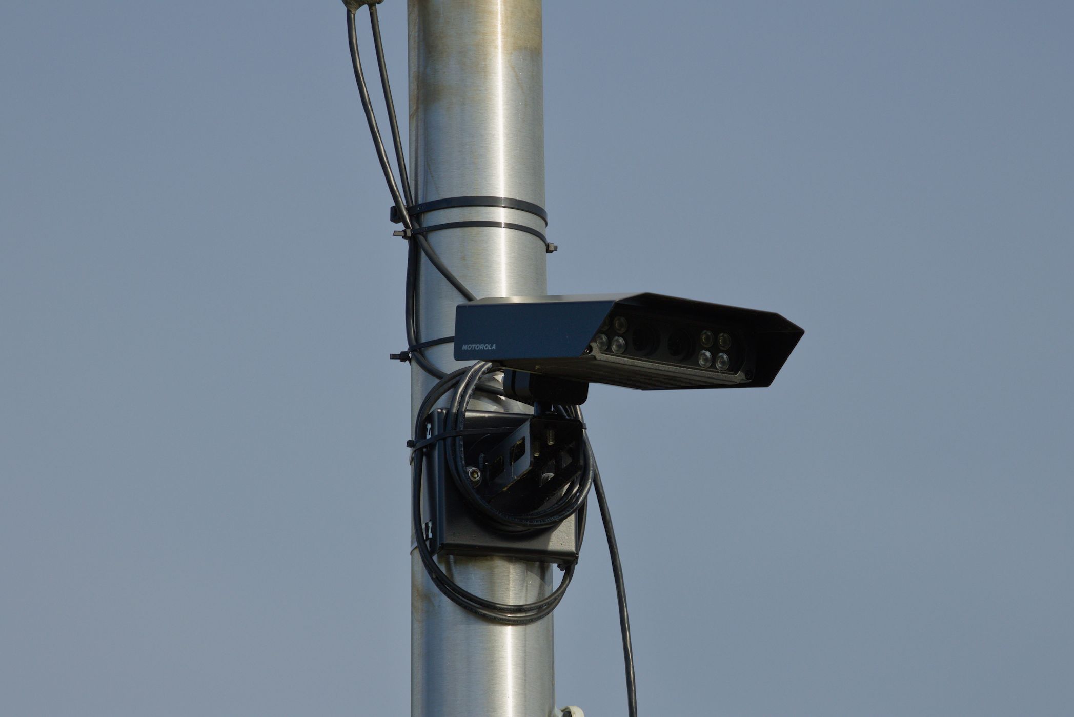 A license plate reader camera mounted on a metal pole against a blue sky.