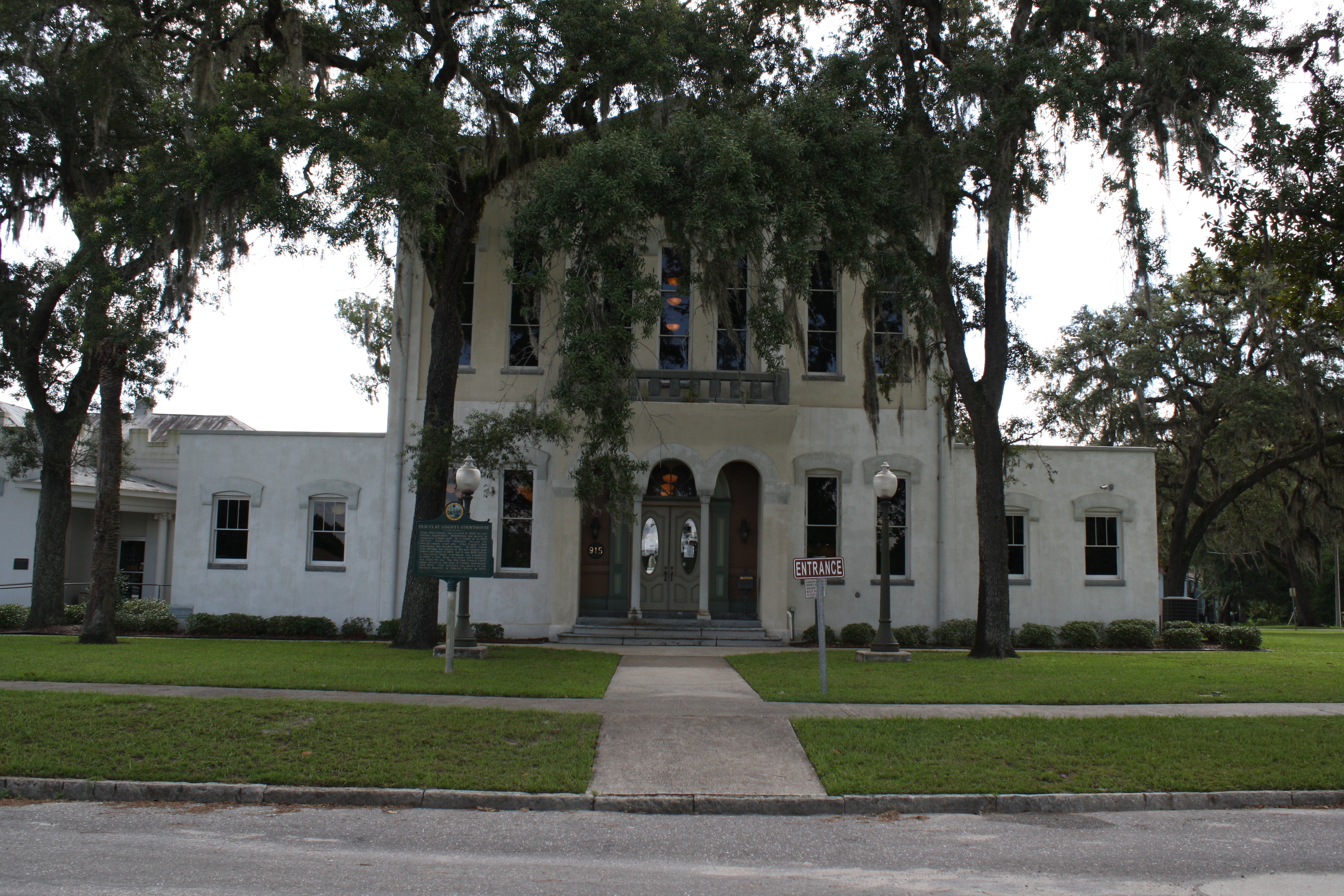Two-story white stucco courthouse building flanked by oak trees draped with Spanish moss.