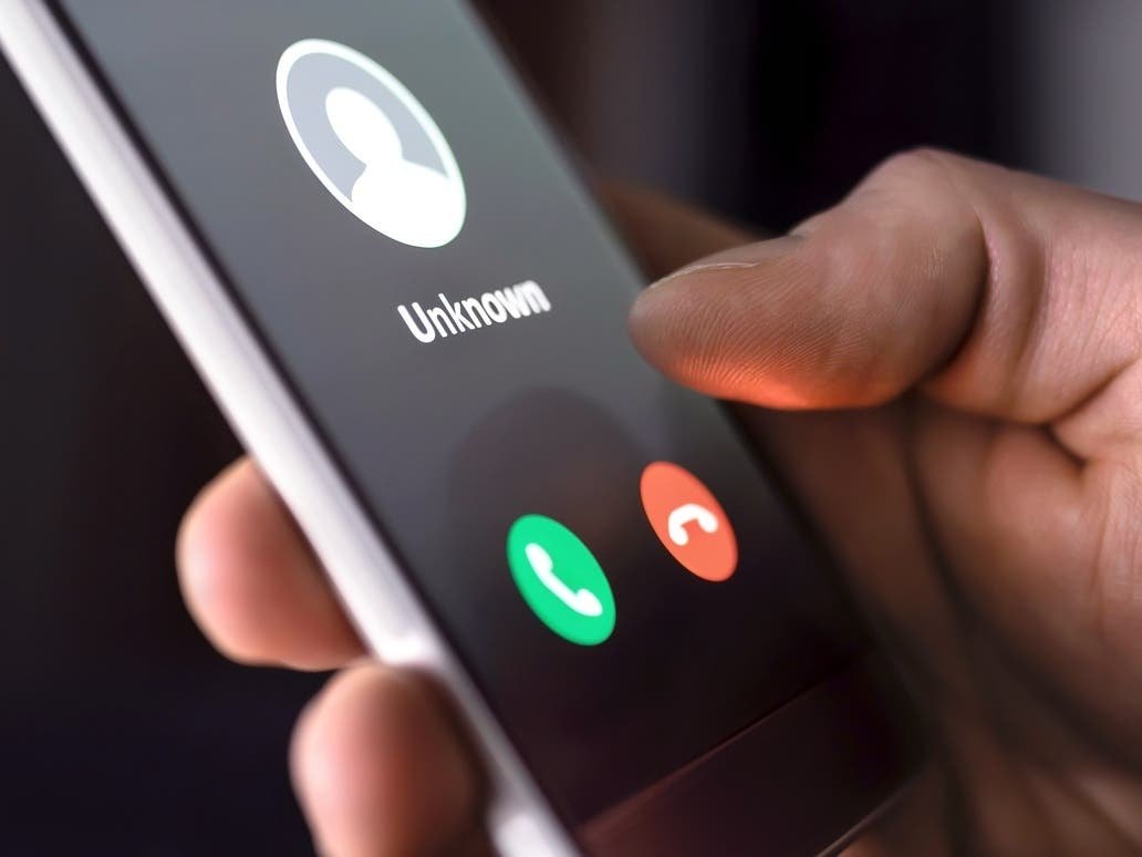 Hand holding a smartphone showing an incoming call from an unknown number.