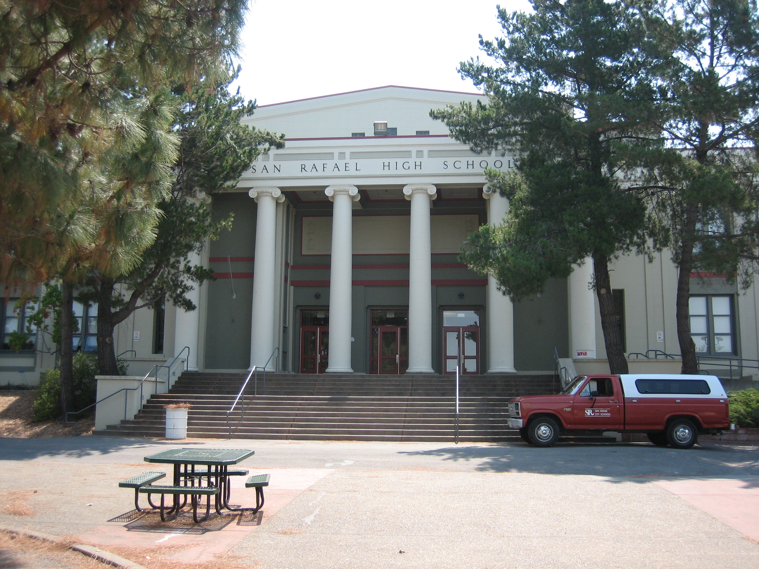 Neoclassical school building with white columns, steps, and picnic tables in front