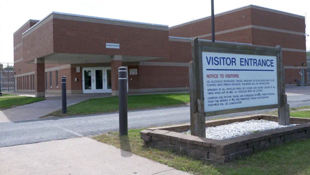 Brick prison building with a visitor entrance sign beside a walkway.