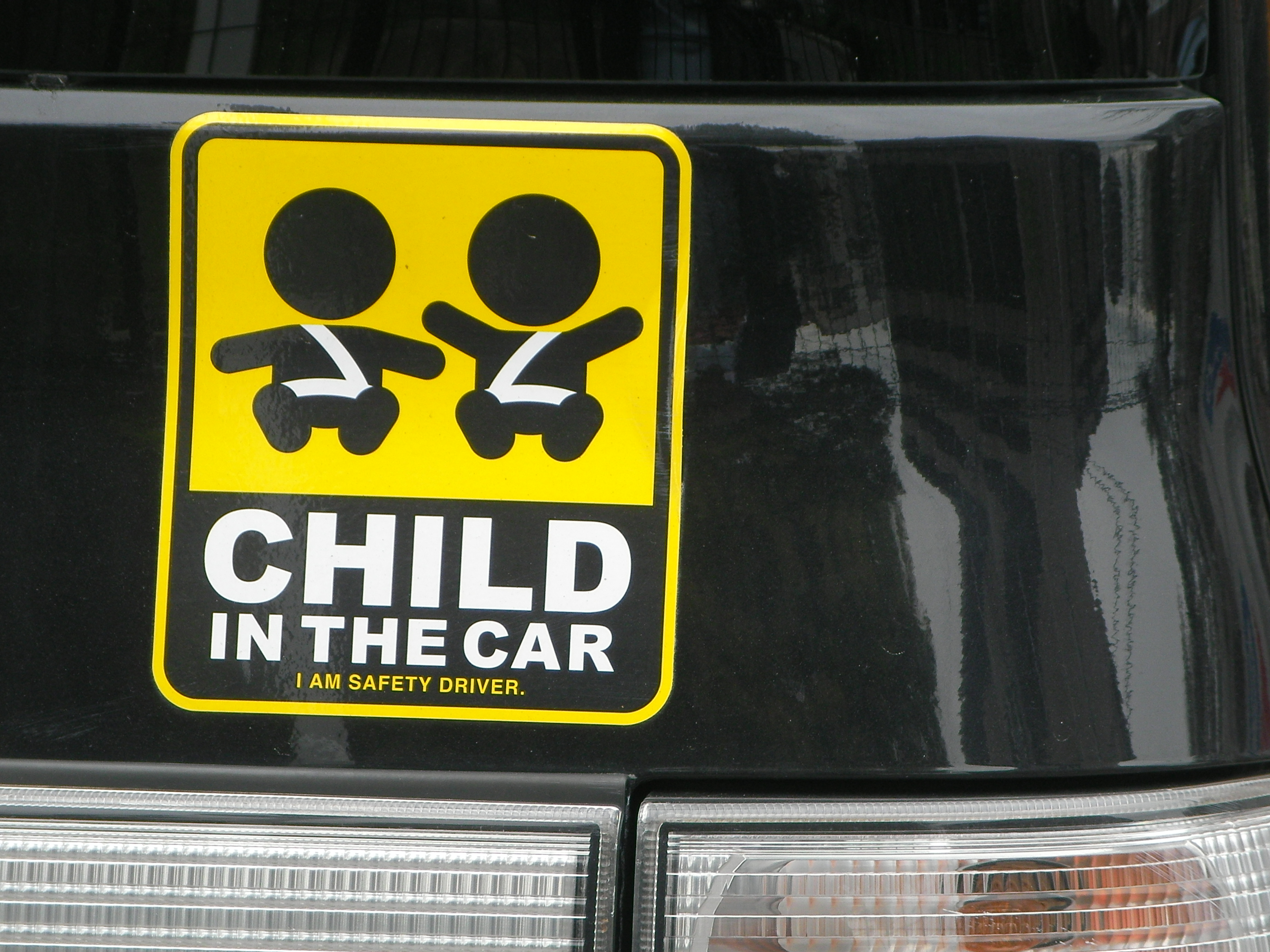Yellow and black child safety sticker on a car's rear window showing two children in car seats.