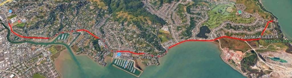Aerial map with a red line marking a road corridor along a bay shoreline.