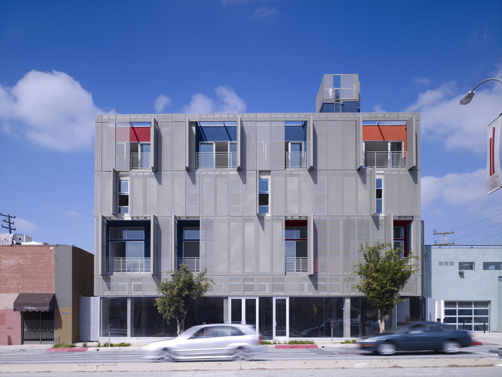 A modern five-story apartment building with a perforated aluminum facade on a city street.